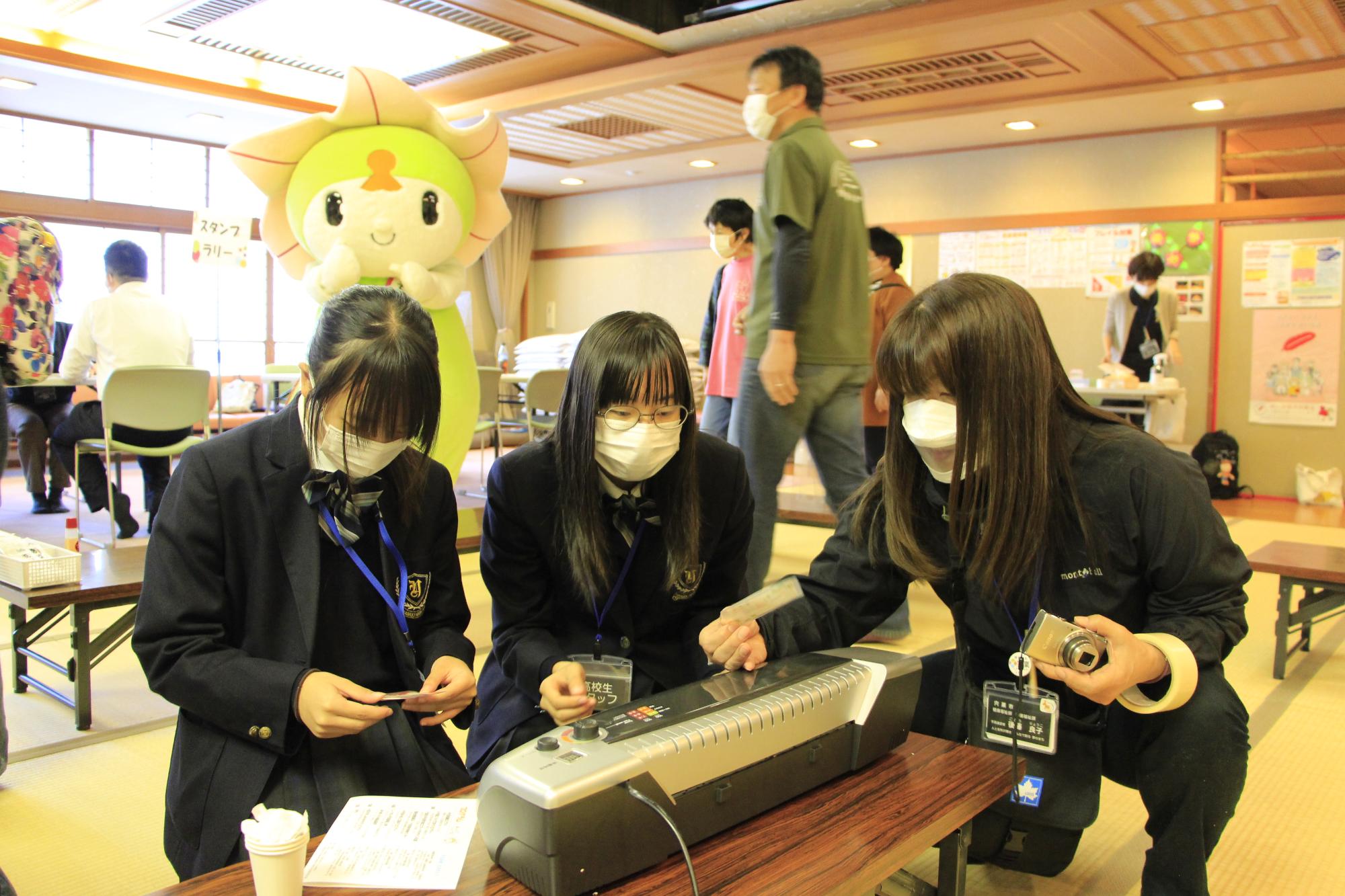 宍粟市手話フェスタの指文字コーナーでボランティアとして参加した兵庫県立山崎高校の生徒らが職員と一緒に来場者のカードを作成している写真