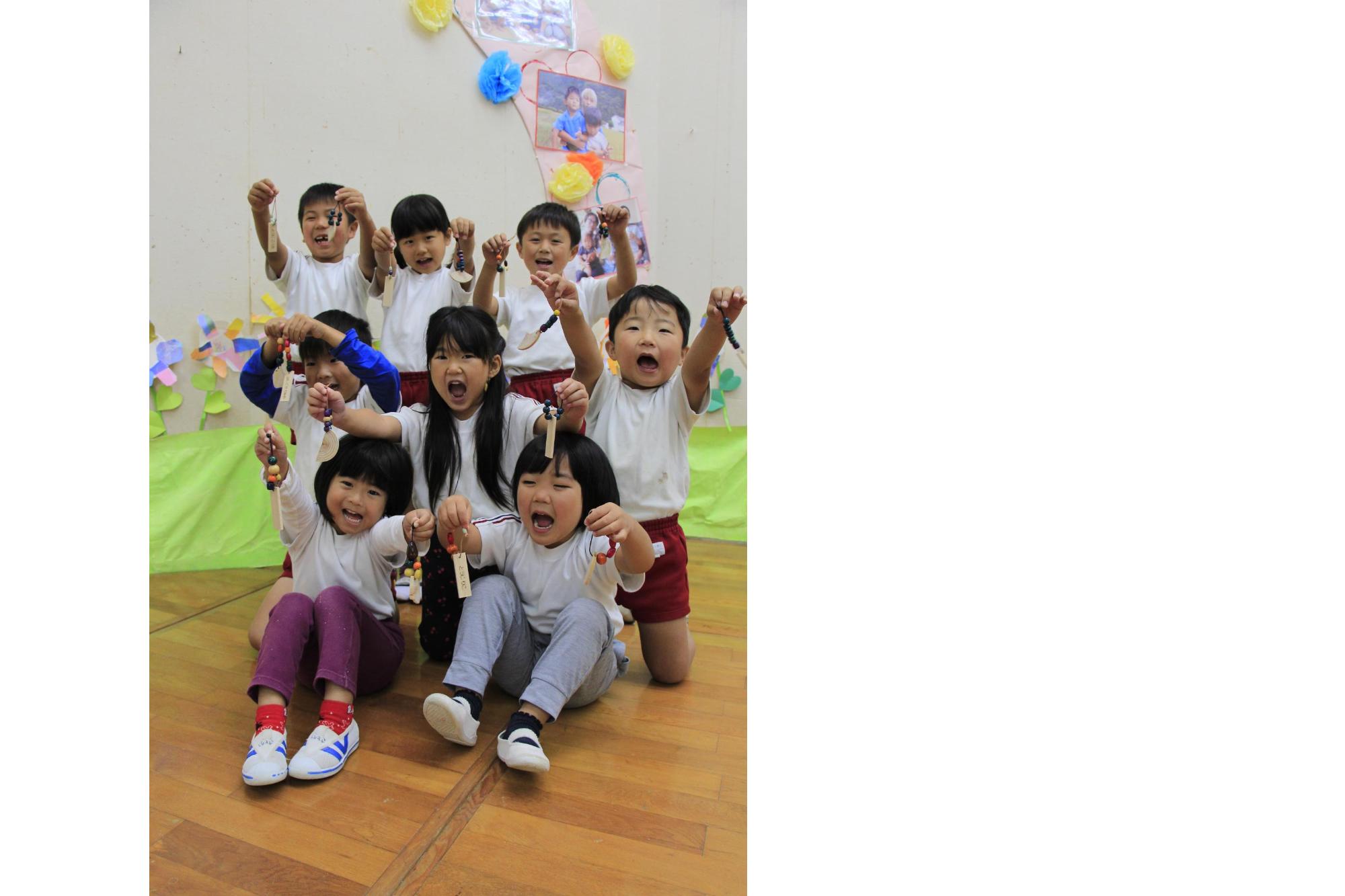 波賀幼稚園の園児ら8人が木でできた手作りキーホルダーを手に持ちはしゃいでいる写真