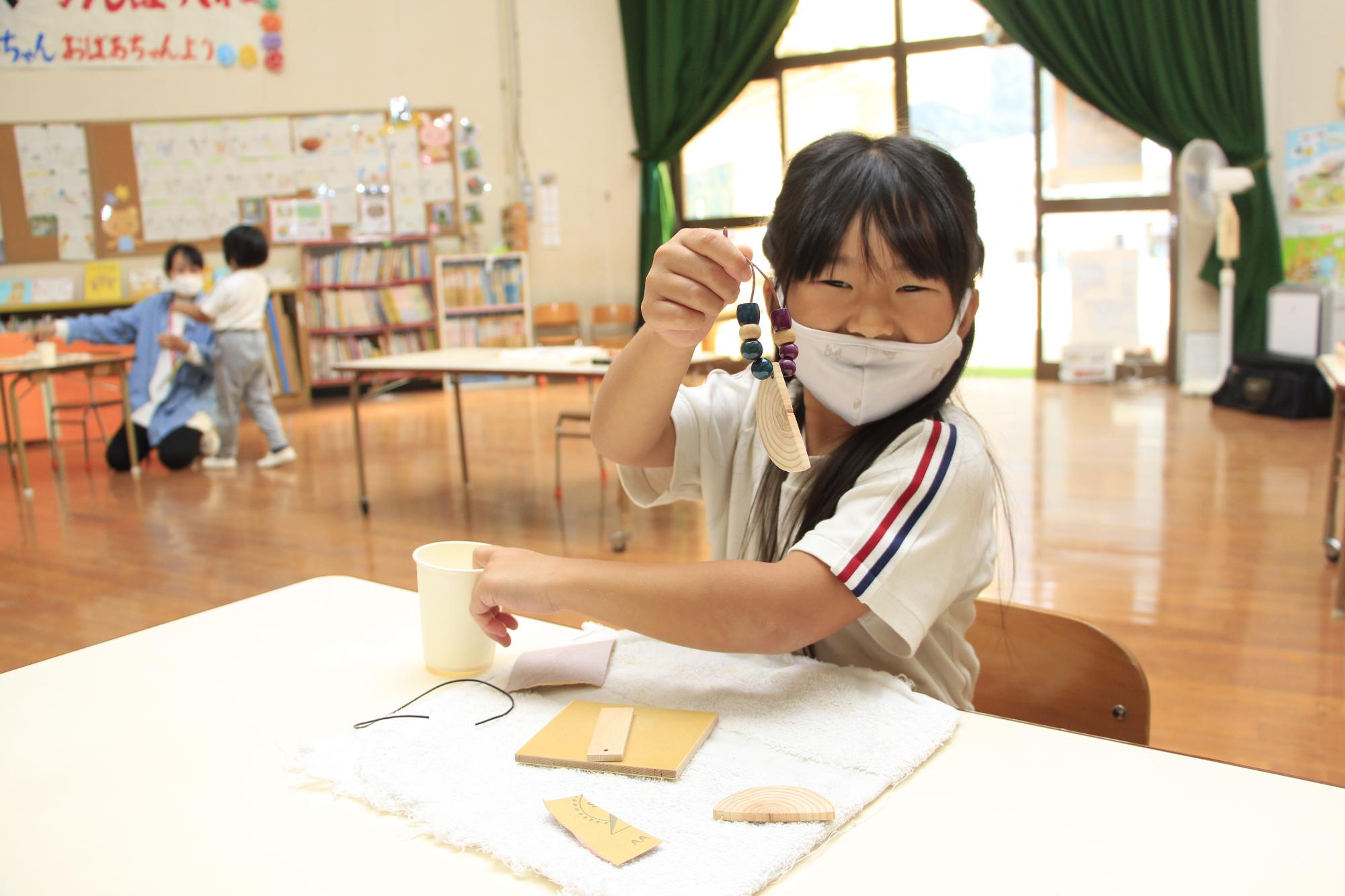 にっこり笑ってできあがったキーホルダーを手に持ち見せてくれている女の子の写真