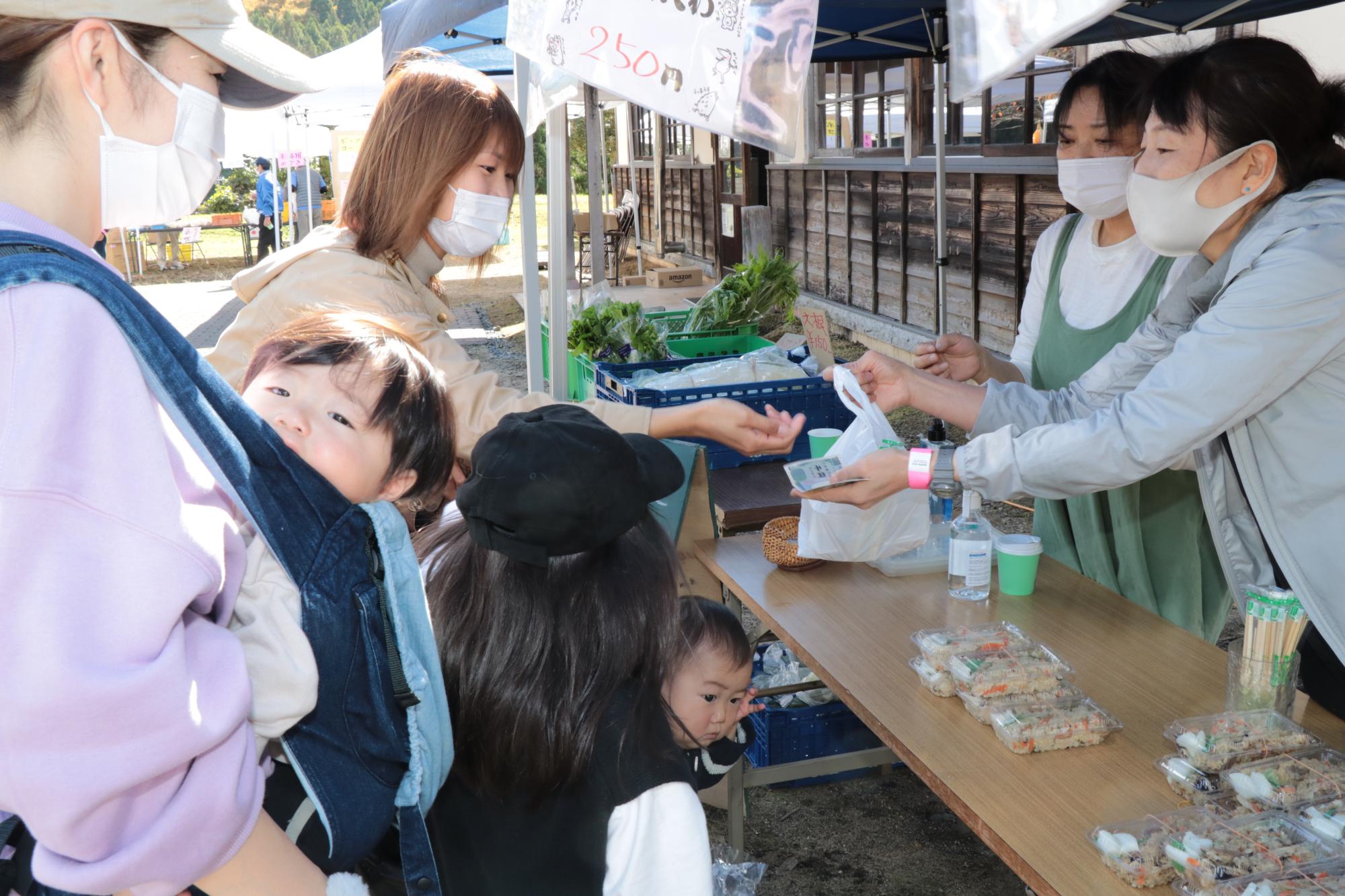 いちのみやふるさとまつり家原遺跡公園会場でパックに入った炊き込みご飯を購入する親子らの写真