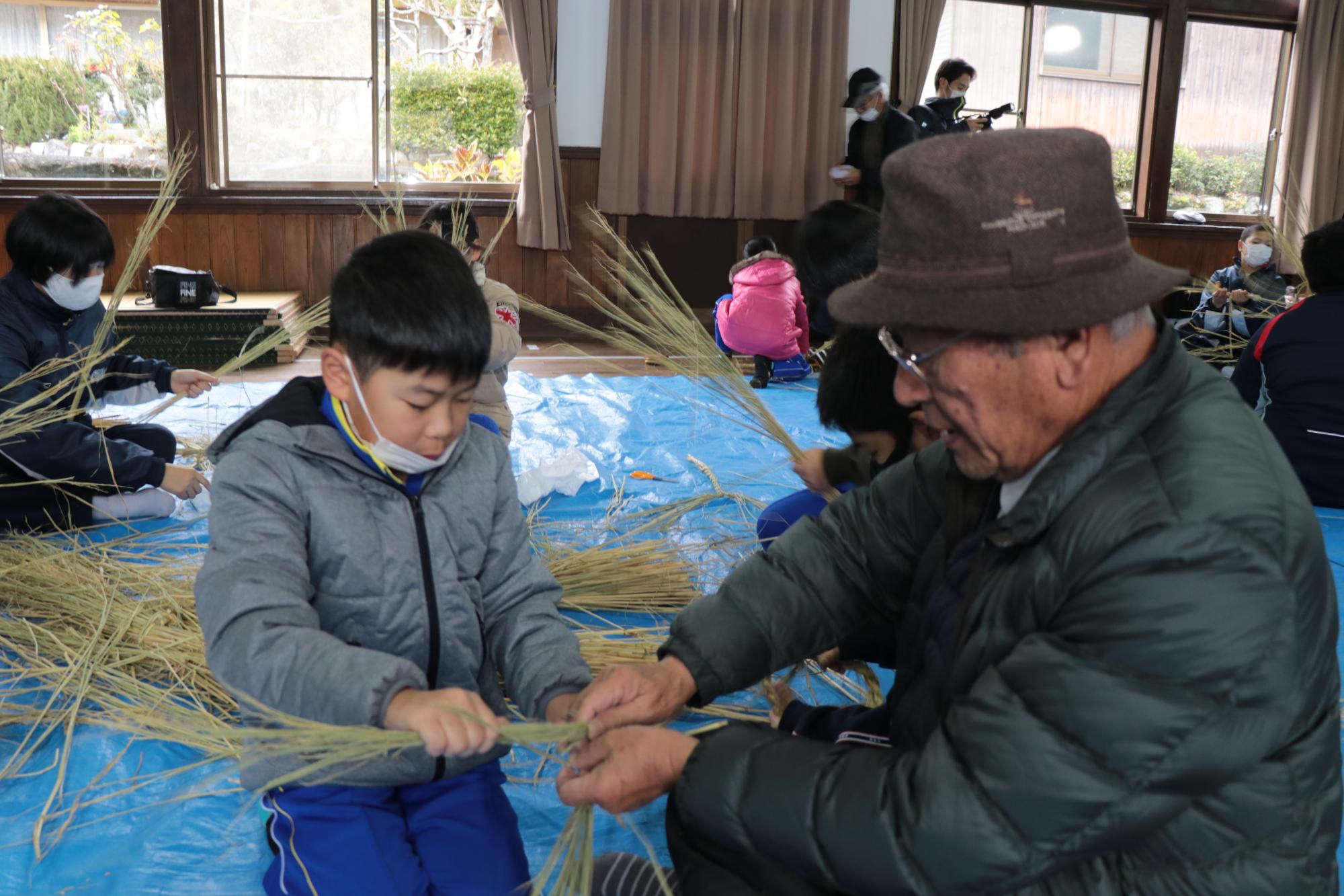 手ほどきを受けながらしめ縄を作る子ども