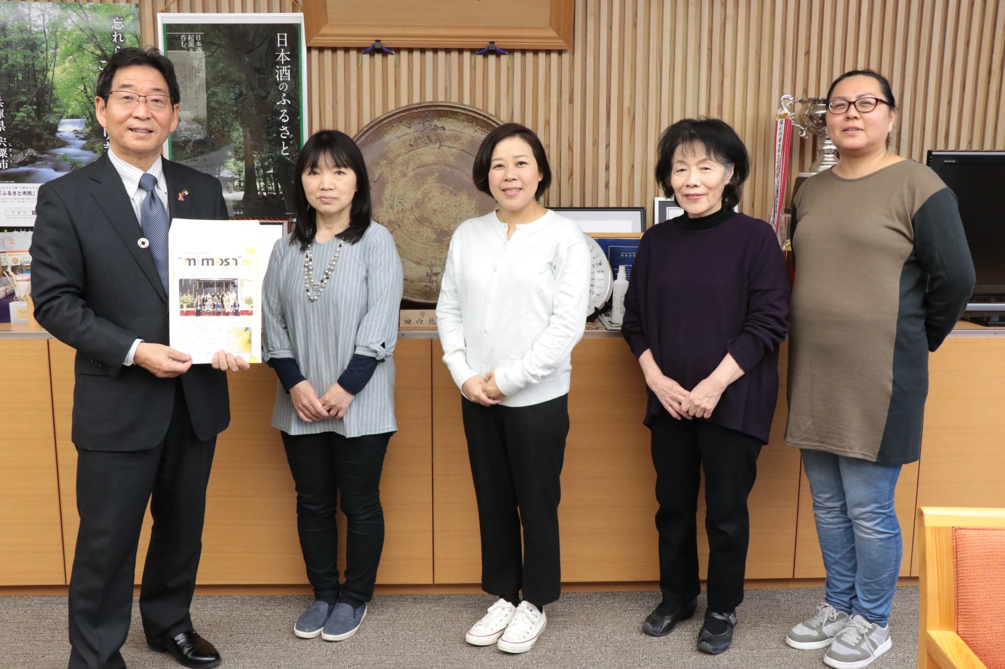 宍粟市役所の市長室でミモザのグループ活動誌を手にする市長とメンバー4人が横一列に並んでいる写真