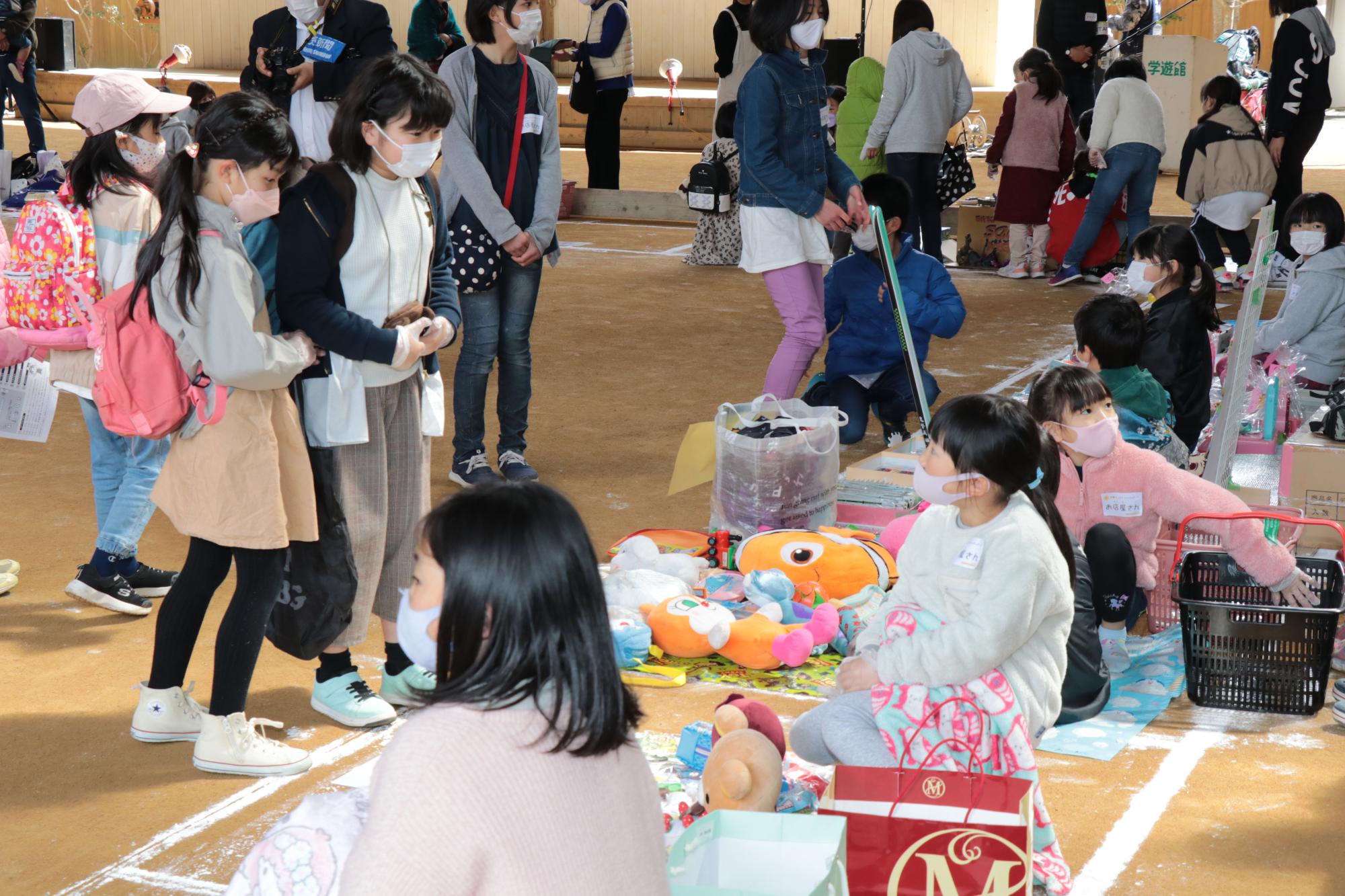 学遊館の会場で店番をする子どもと商品を買いに来た子どもの写真