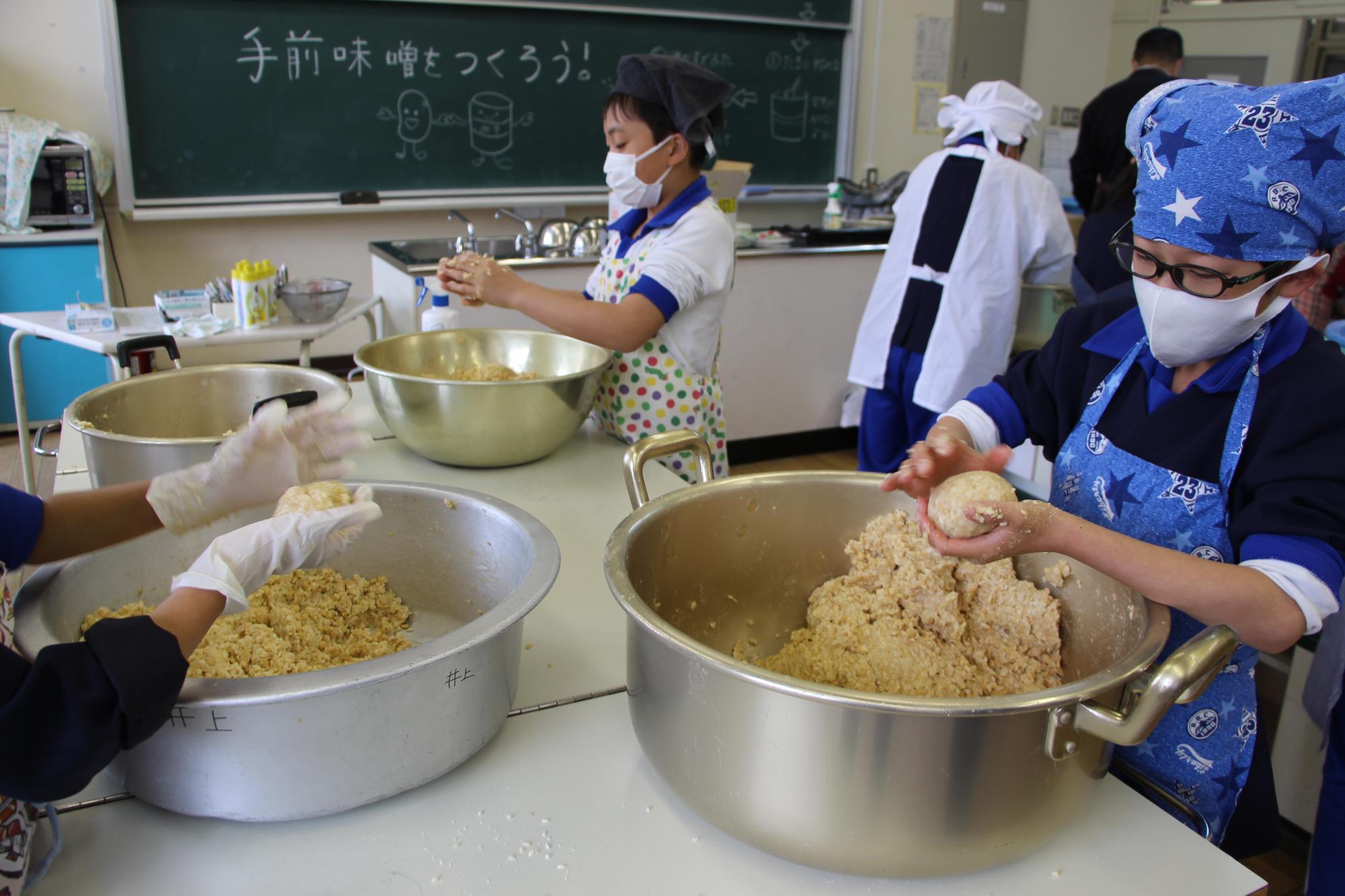 神野小学校の調理室でつぶした大豆を丸めてみそ玉を作る子どもの写真