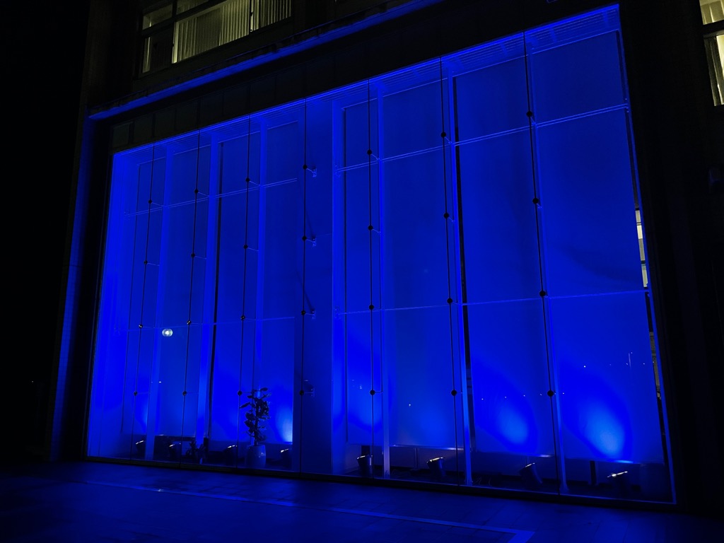屋外から青色に光って見える市役所1階の市民ロビーの写真
