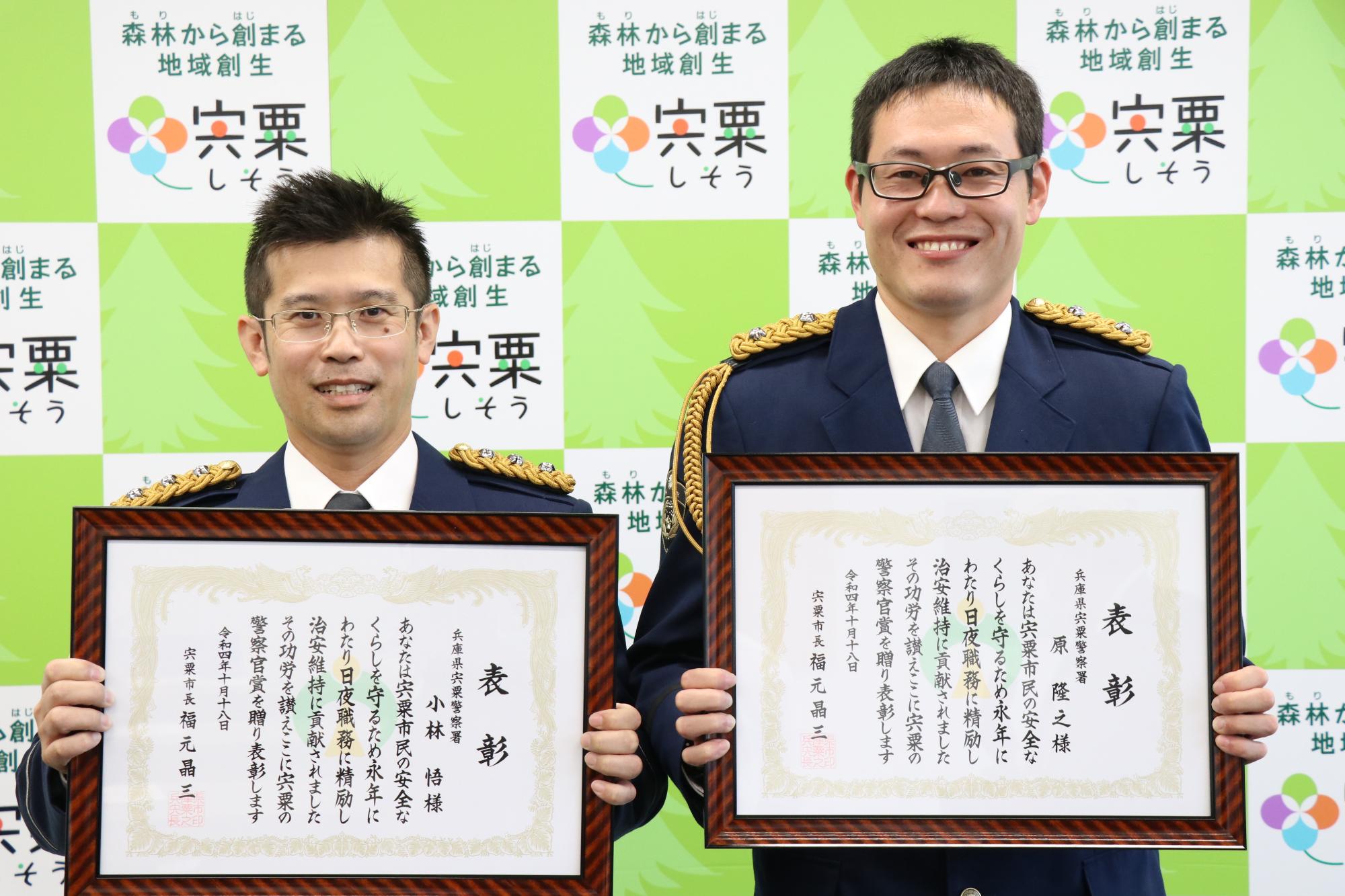 宍粟の警察官賞の表彰状を胸の前に掲げ、並んで笑顔を見せている兵庫県警宍粟署交通課の小林悟巡査部長と同地域課の原隆之巡査長の写真