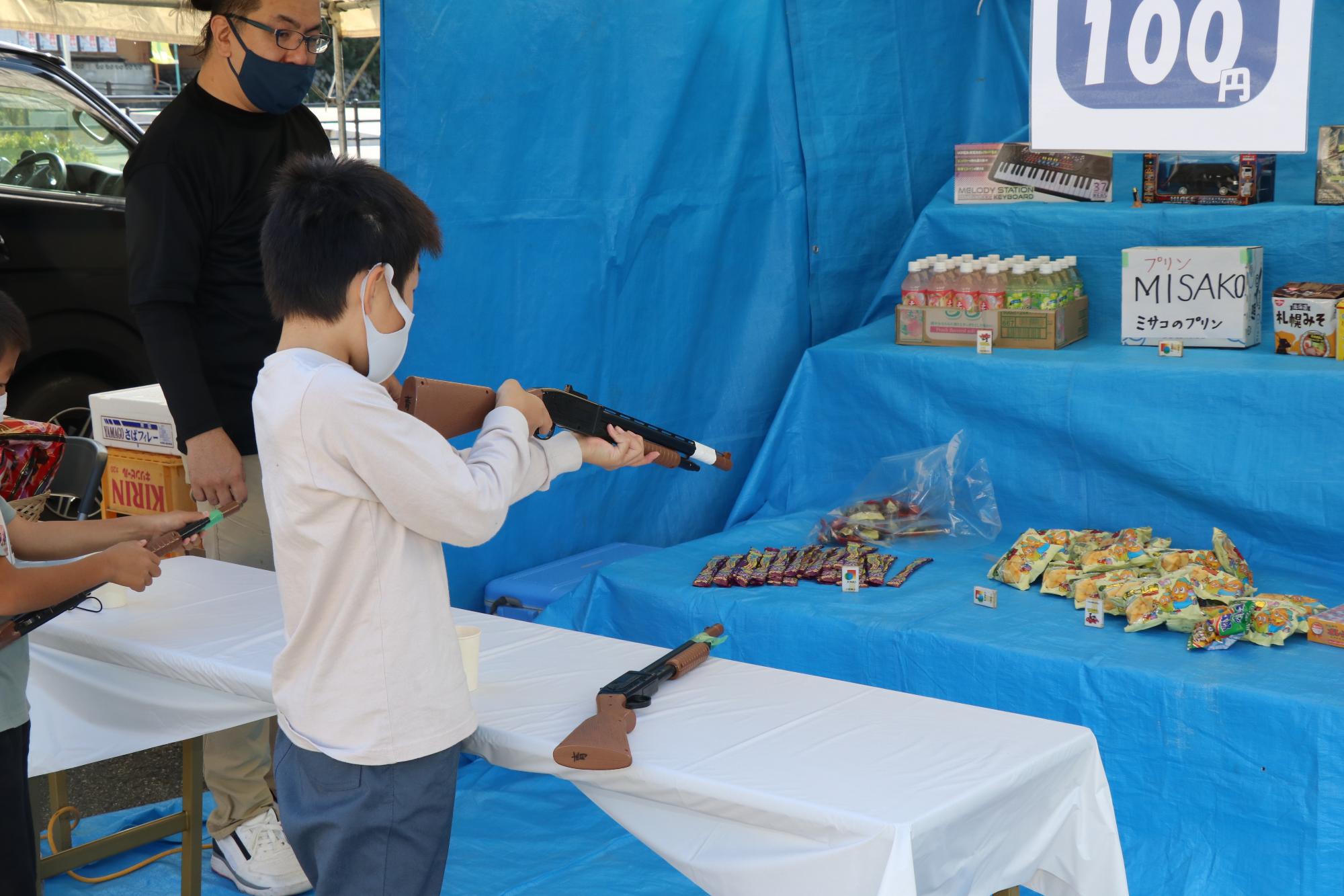 射的ゲームで子どもがおもちゃの銃を構えて的を狙っている写真