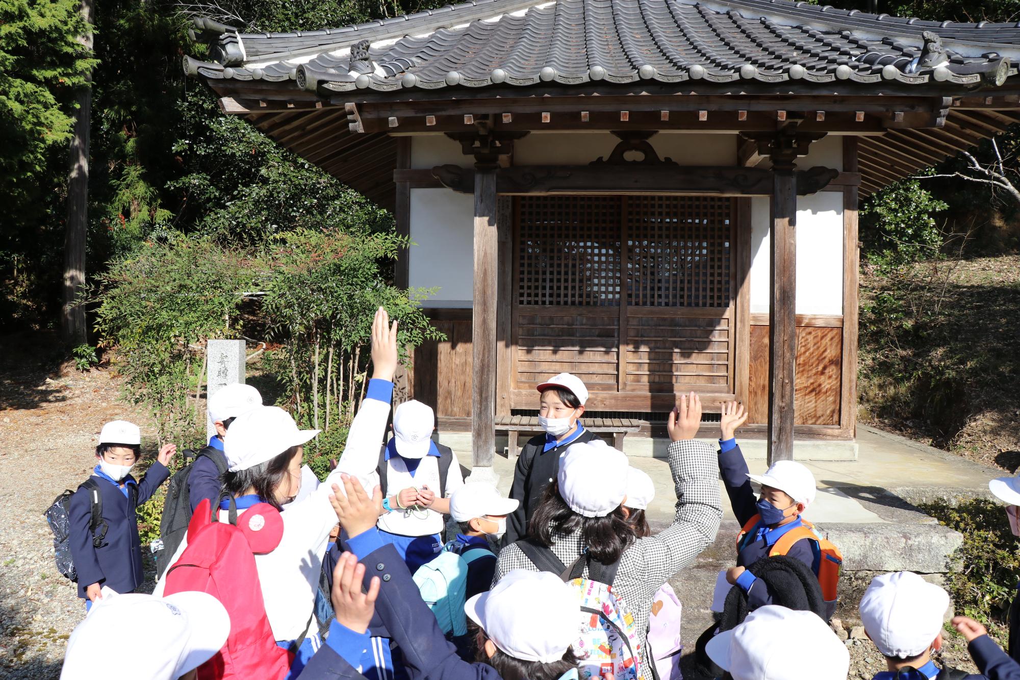 川戸地区にある薬師堂の前で6年生が出したクイズに手を挙げて答える児童らの写真