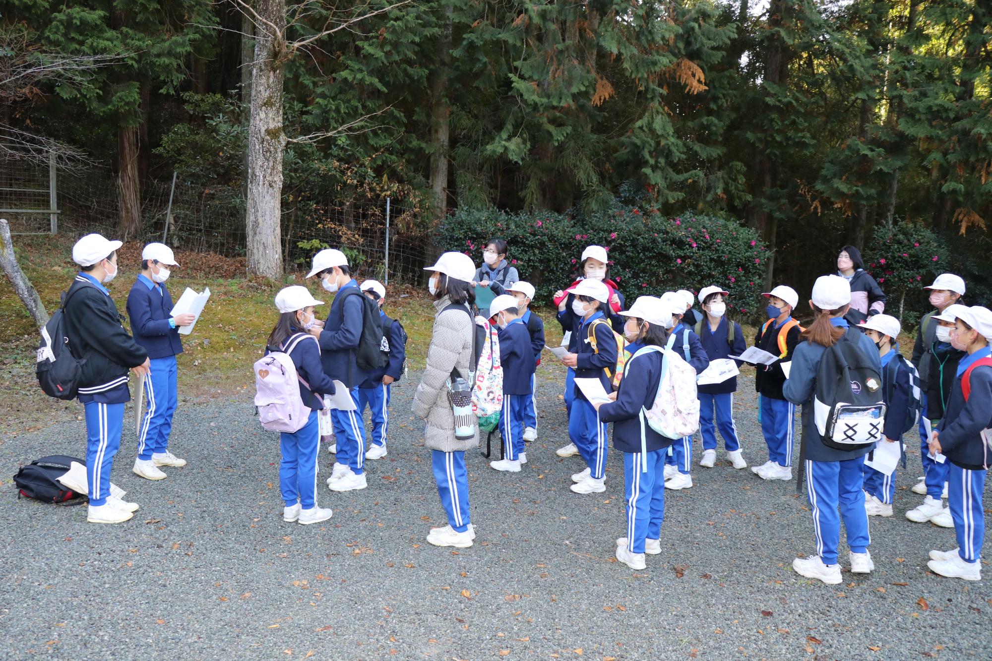 川戸地区内で地元の神社について解説する6年生とそれを聞く下の学年の児童らの写真