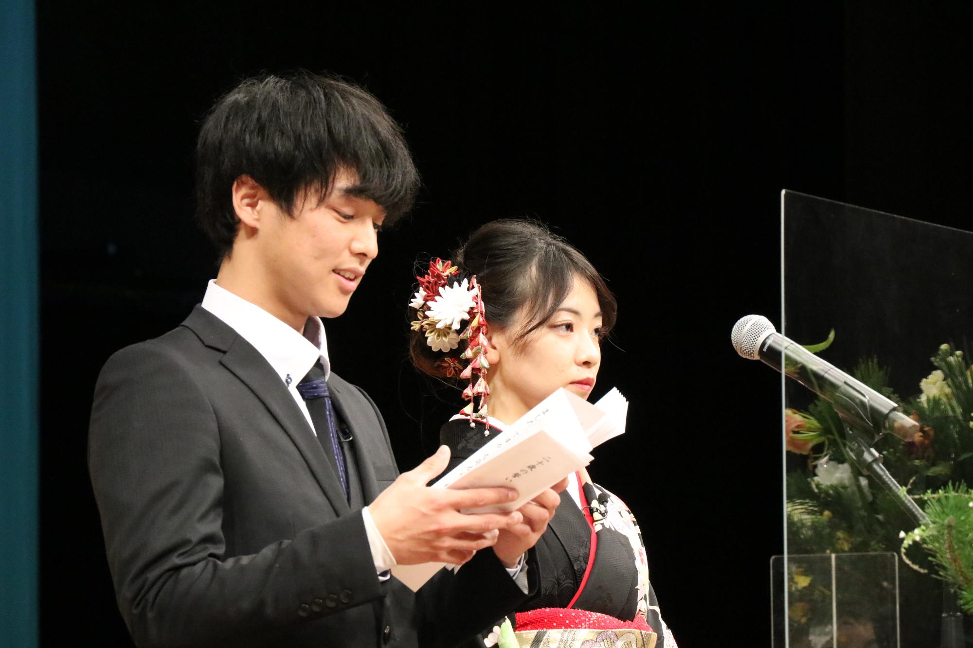 山崎文化会館のステージ上で新成人らに向かって誓いの言葉を述べる平瀬竜己也さんと森脇美海さんの写真