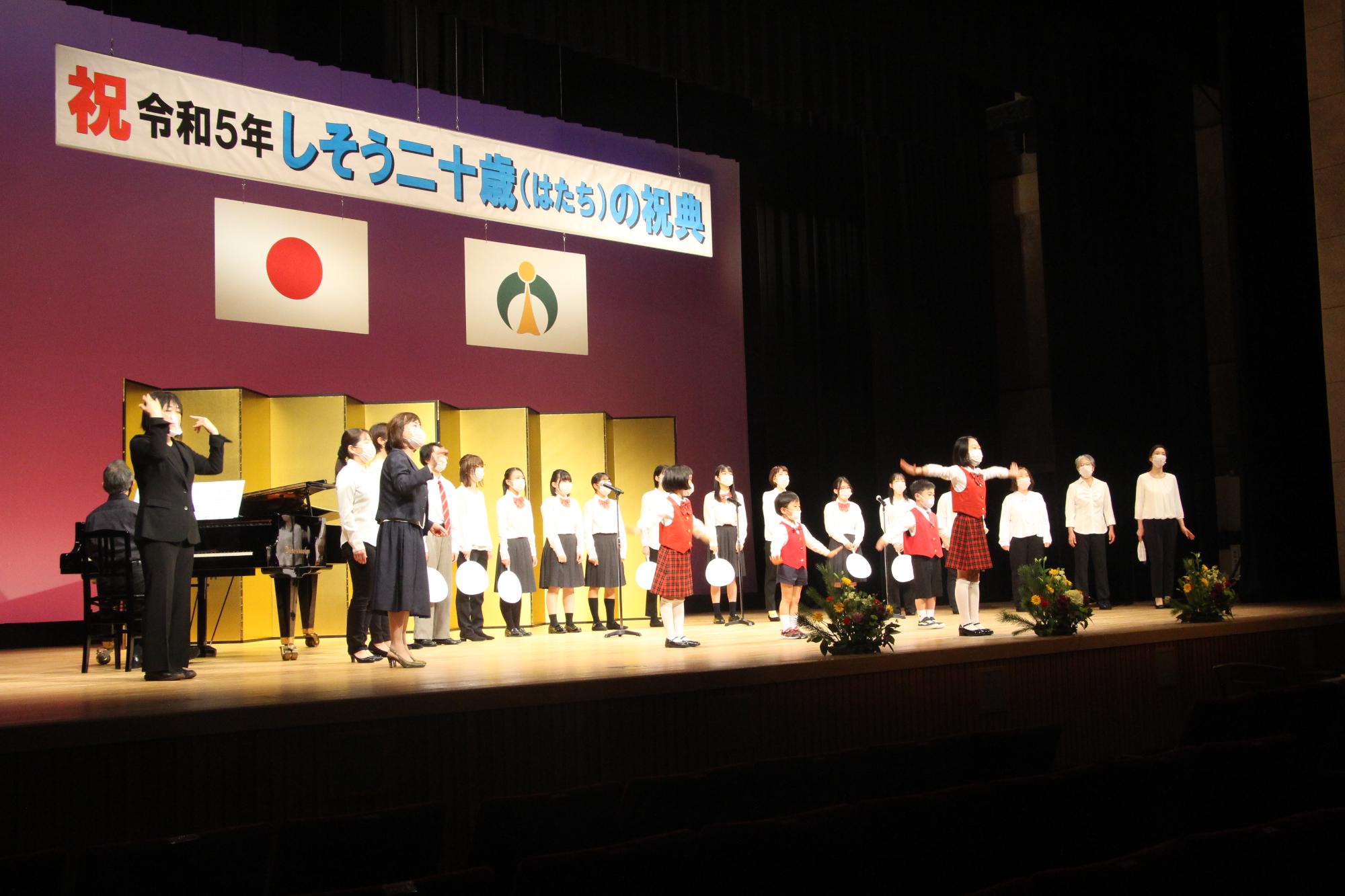 山崎文化会館のステージ上で新成人らを祝う合唱を披露する宍粟市少年少女合唱団の写真