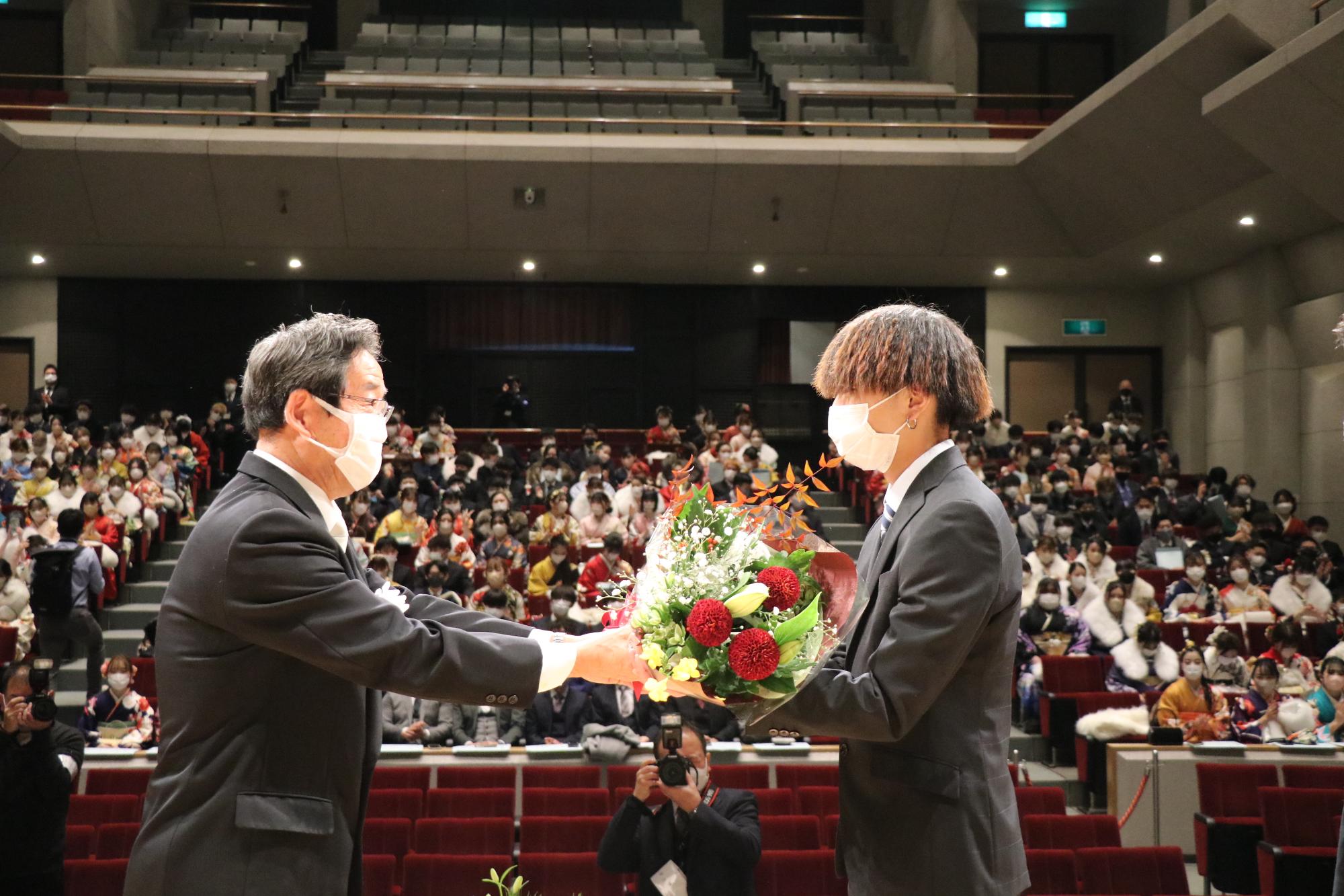 山崎文化会館のステージ上で新成人を代表して、市長からお祝いの花束を受け取る上垣翔太さん