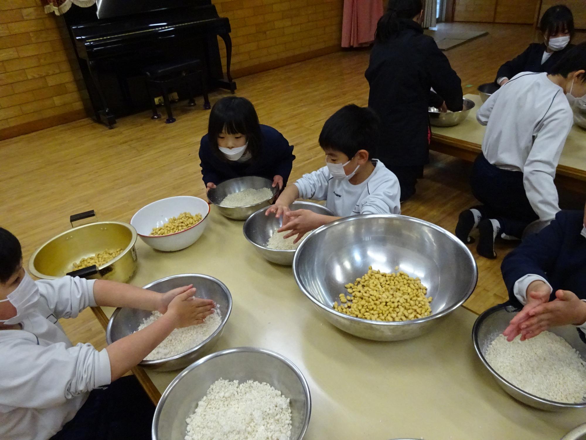 児童らがテーブルの上に大豆や麹が入ったボールを並べている写真
