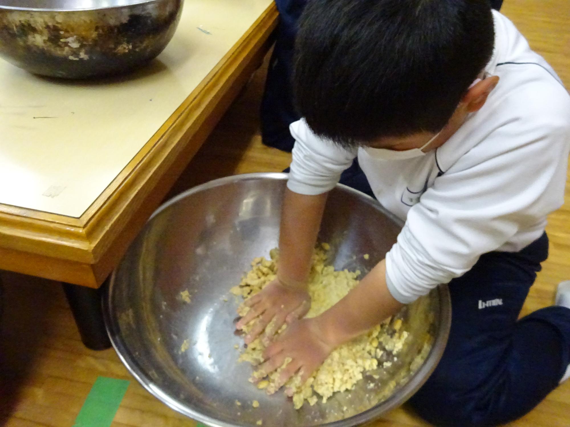 一つのボウルに入った大豆や麹などを児童が両手で混ぜ合わせている写真