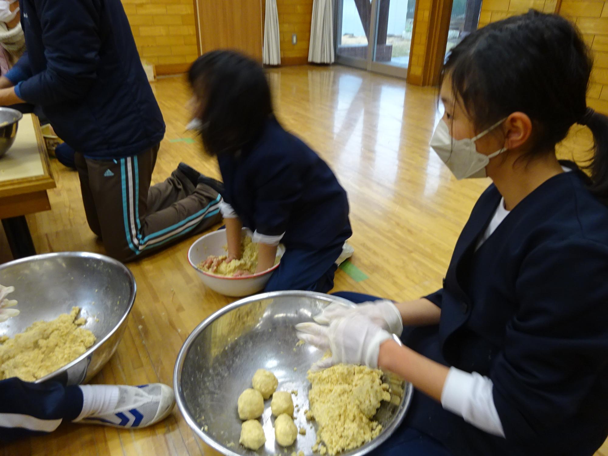 児童らが大豆と麹を混ぜ合わせたり、混ぜ合わせた後に空気抜きのため団子状に丸めたりしている写真