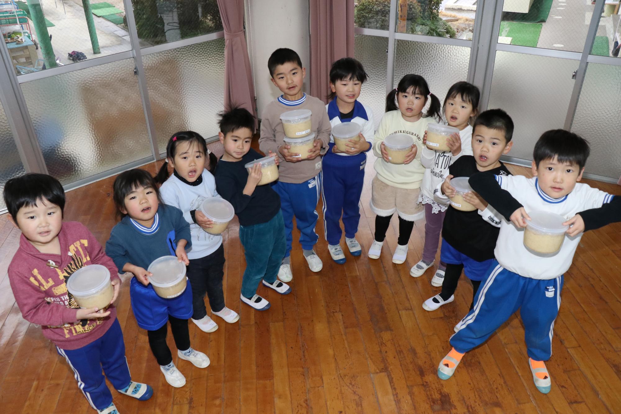 河東幼稚園で仕込み終えたみそを手に持ち並んでいる園児らの写真