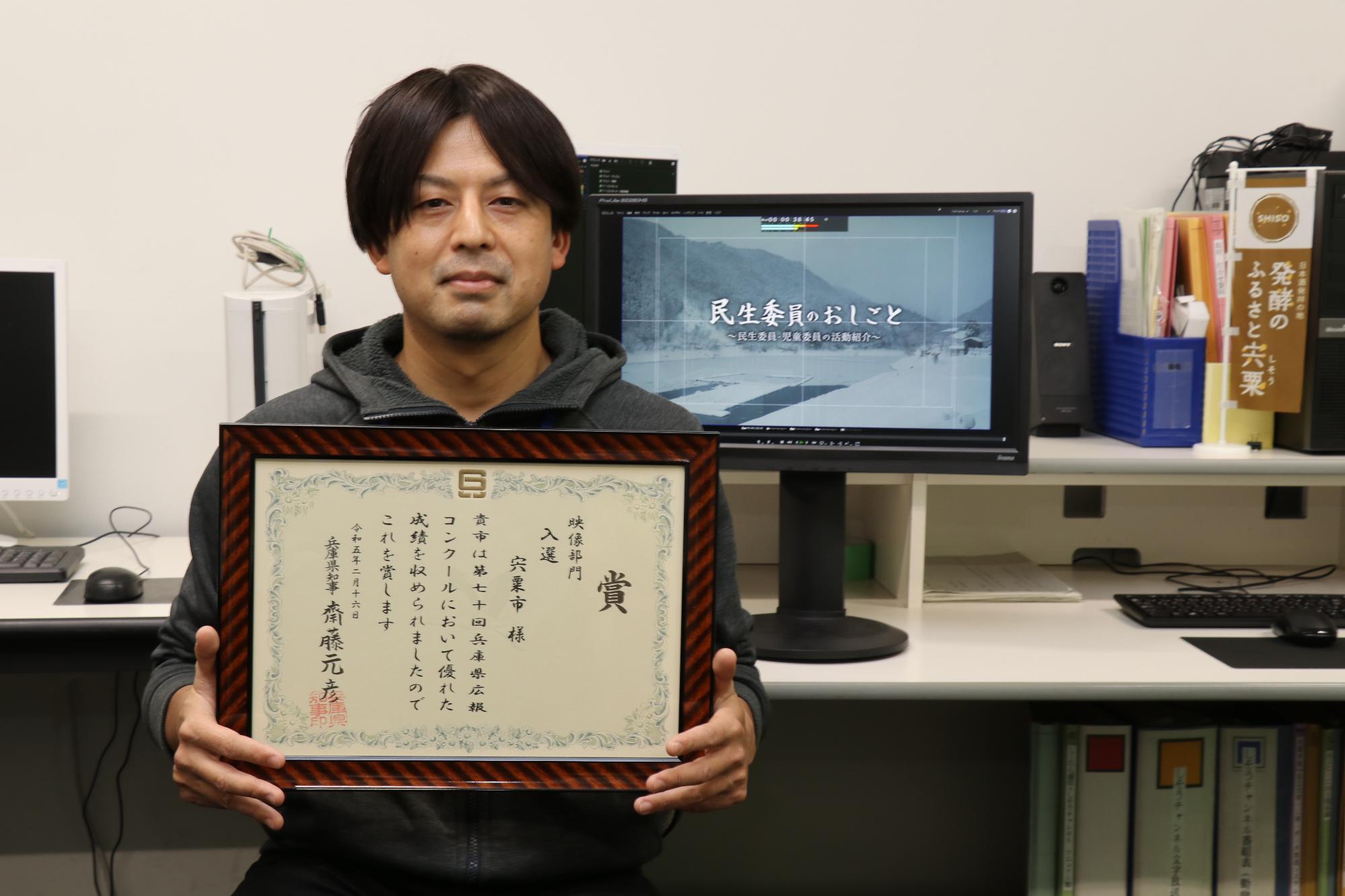 兵庫県広報コンクールで入選した番組を制作した山内さんが賞状を手に笑顔を見せている写真