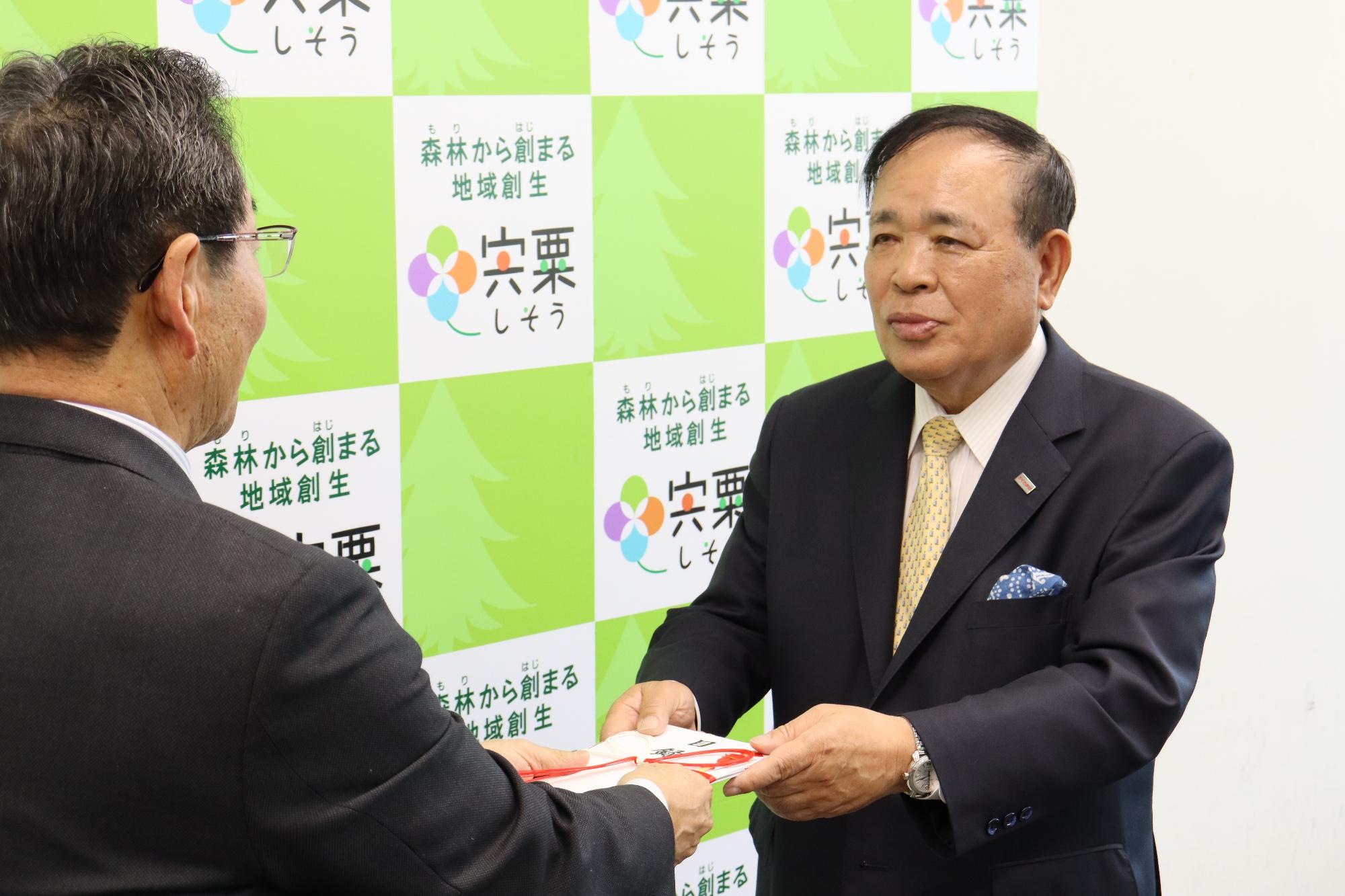 幸南食糧株式会社取締役会長の川西修さんが宍粟市長に寄付金の目録を手渡している写真