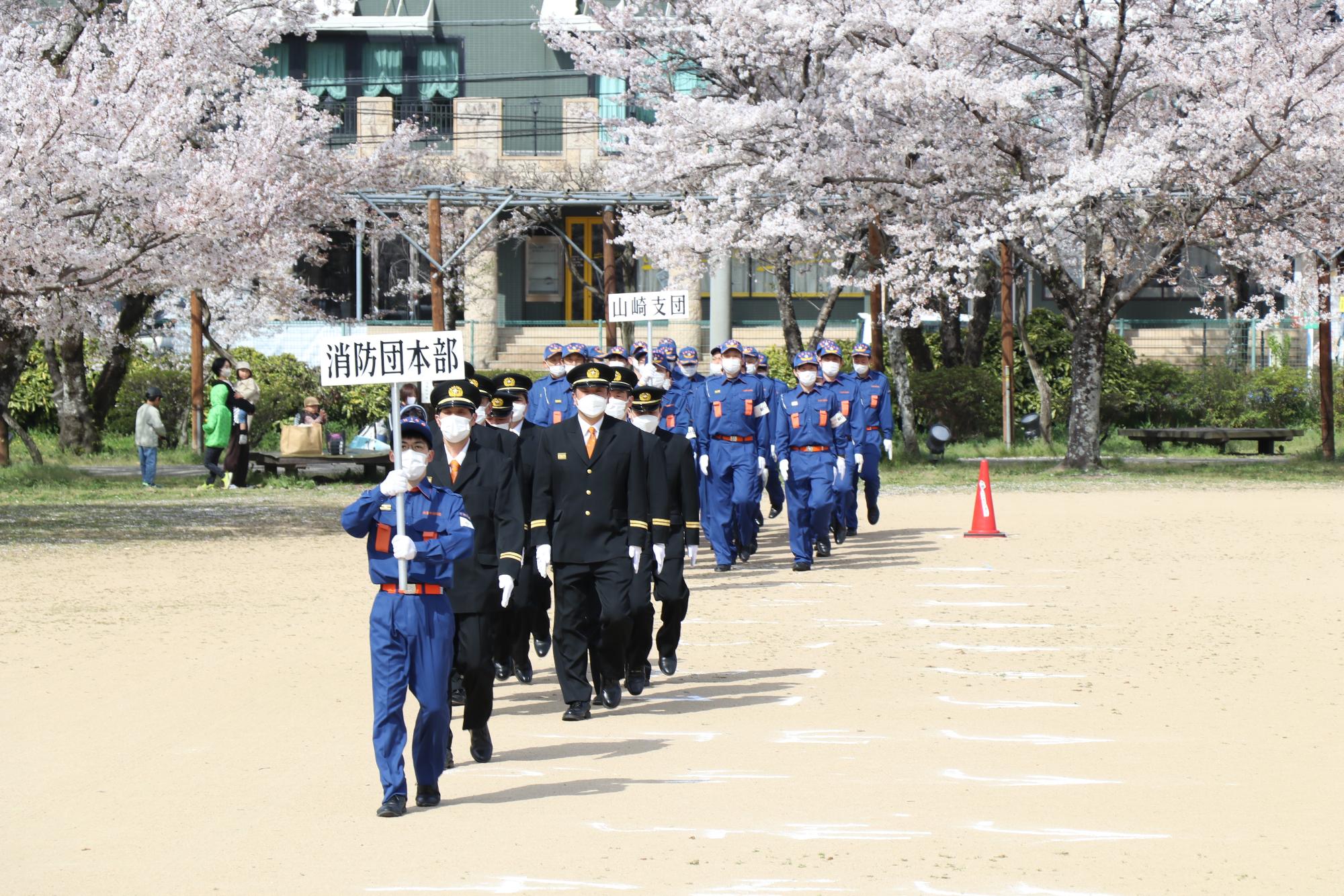 夢公園の会場で各分団ごとに行進をする消防団員らの写真