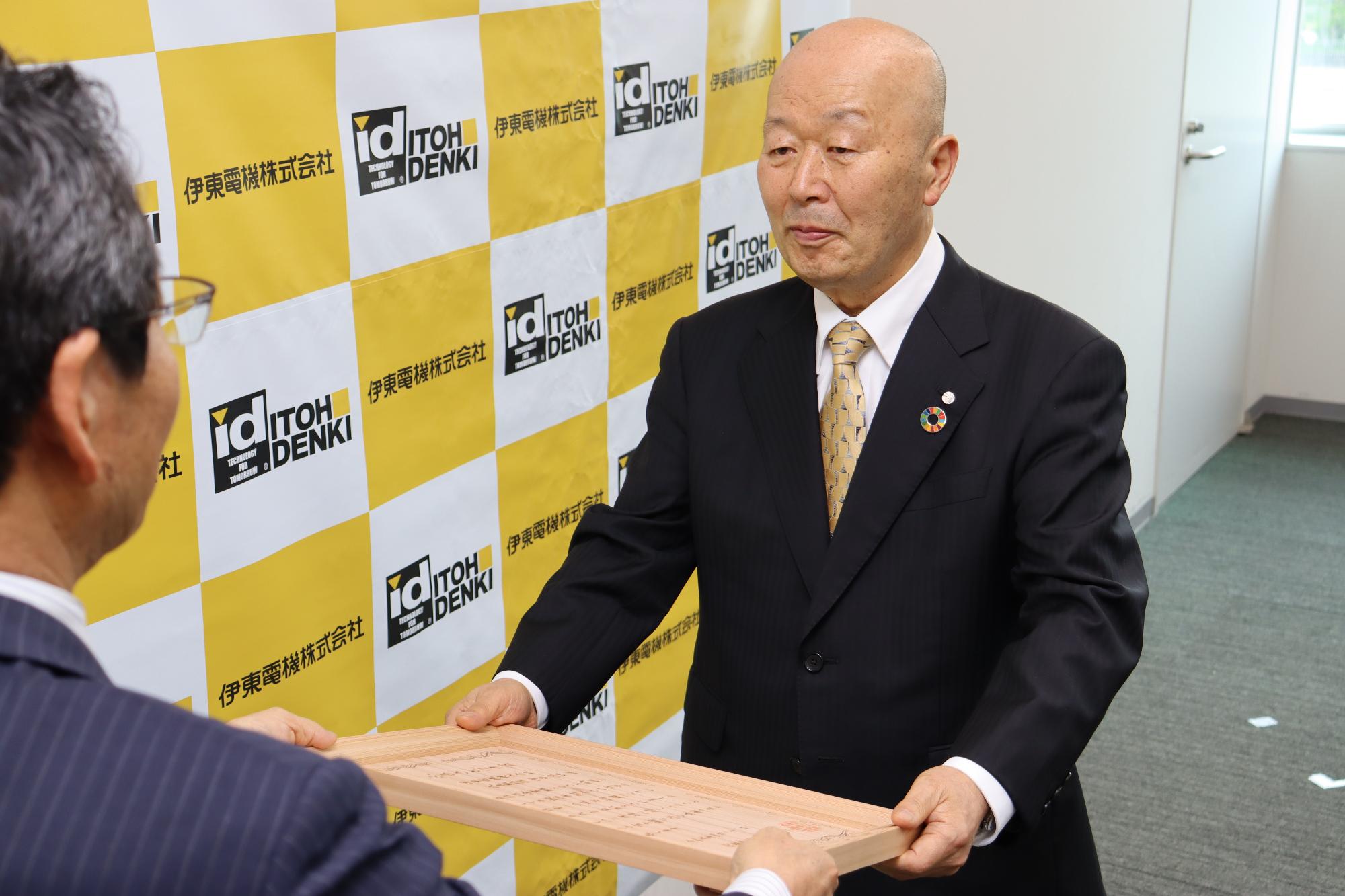 福元市長から伊東電機の伊東一夫代表取締役会長が木製の賞状を受け取っている写真