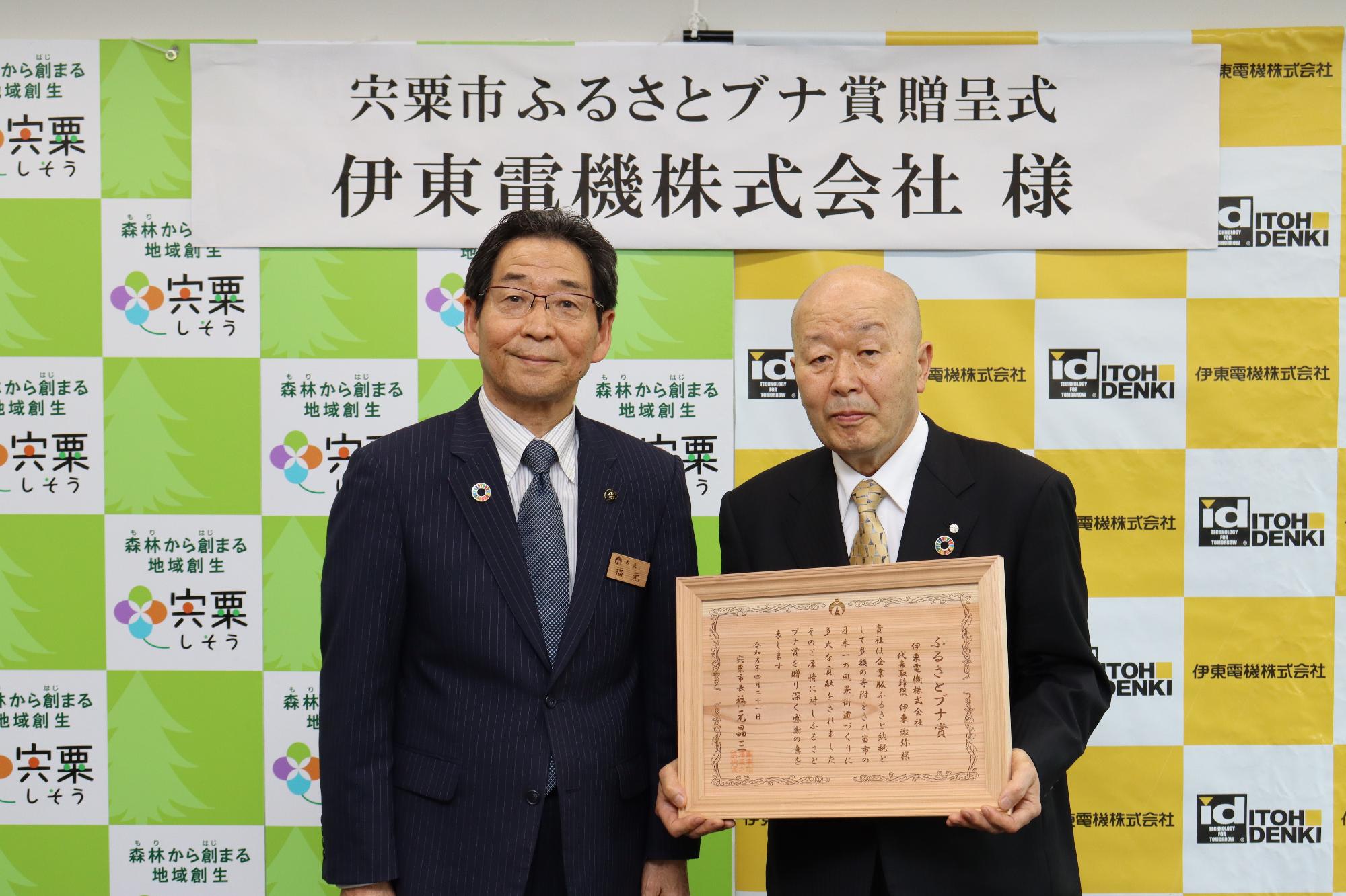 伊東電機の代表取締役会長 伊東一夫さんがブナ賞の木製の賞状を持ち、福元市長と並んで立っている写真