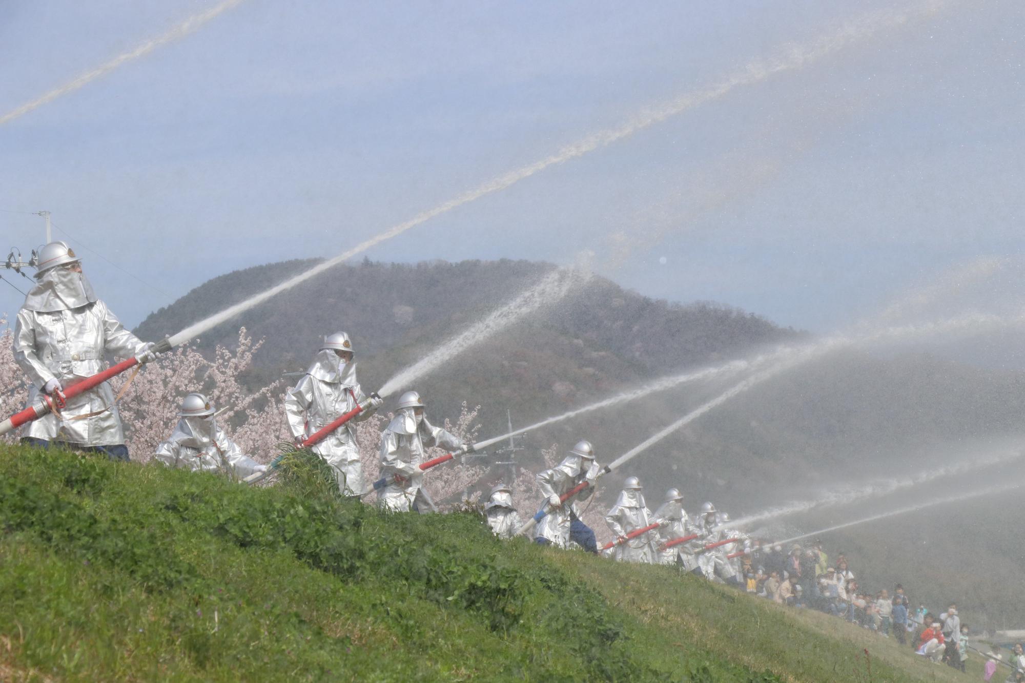 市役所隣のせせらぎ公園の土手から揖保川に向かって放水する消防団員らの写真