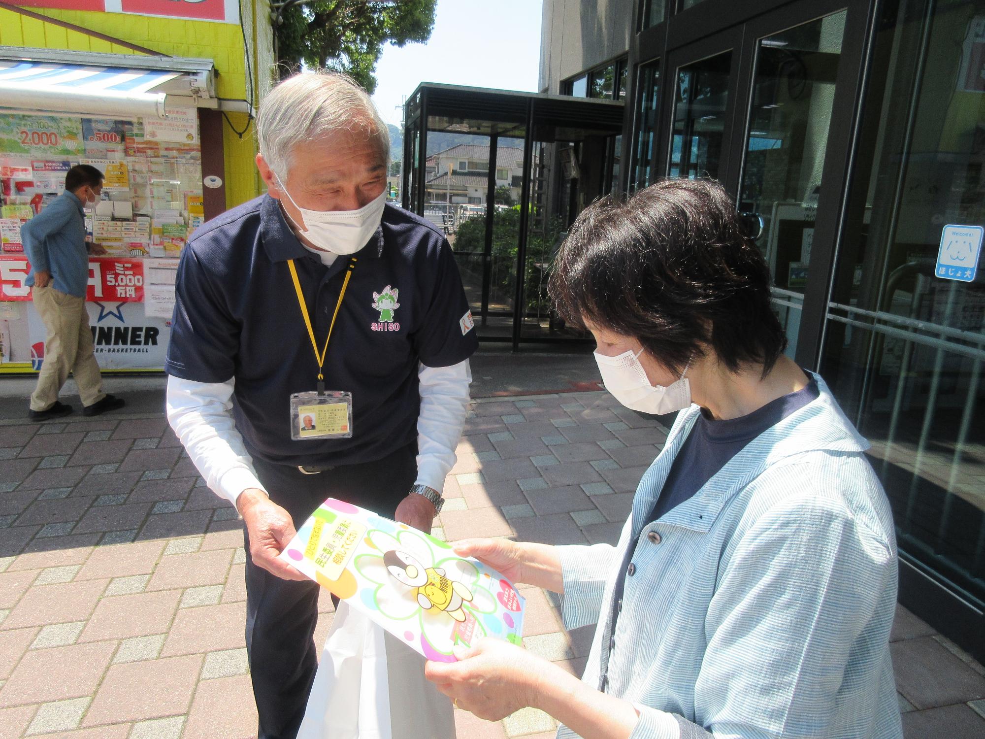 市の民生委員・児童委員がイオン山崎店の店内出入口周辺で客にチラシを配っている写真