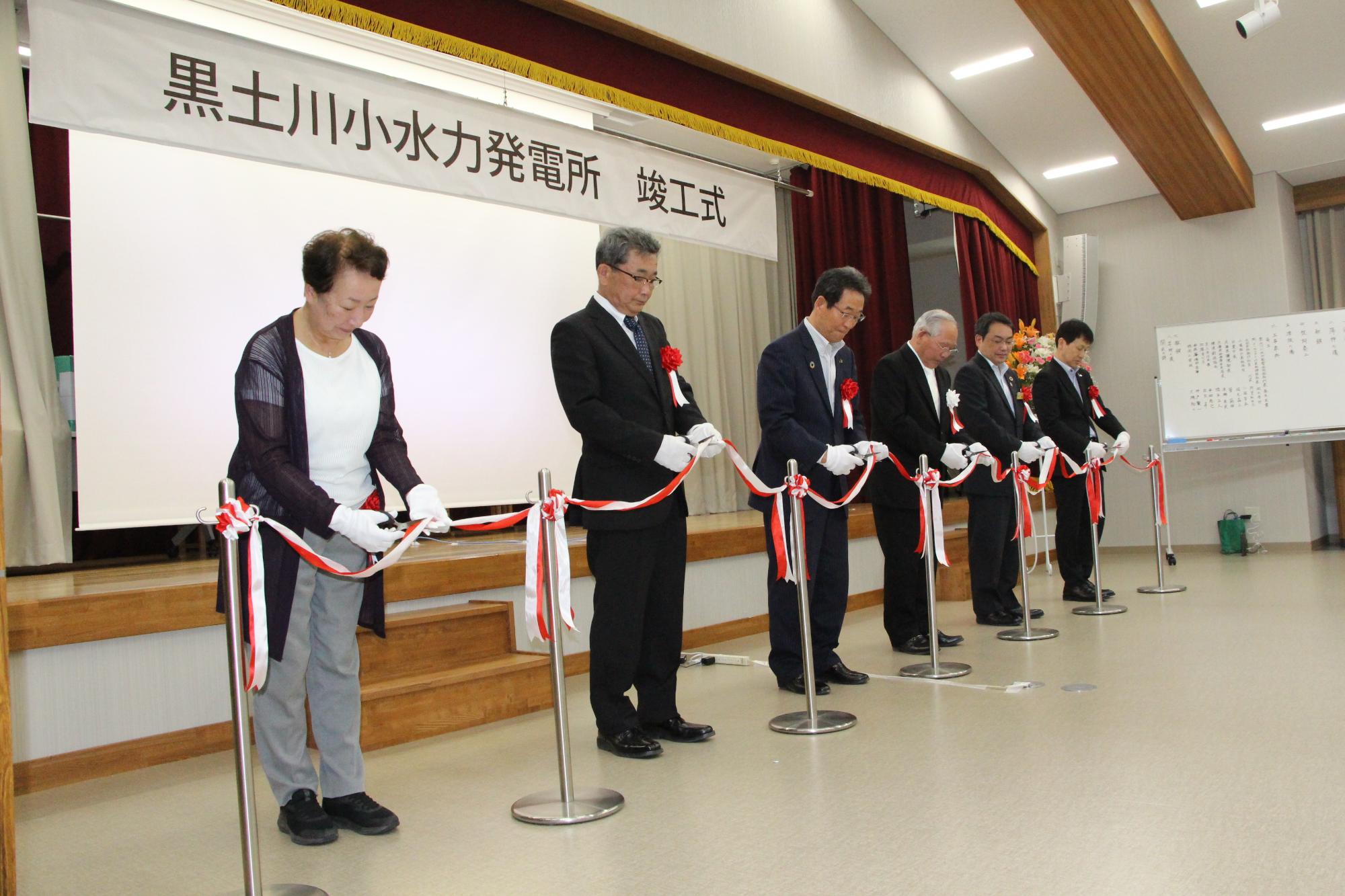 ライブリーちくさで開かれた「黒土川小水力発電所」の竣工式で、関係者らがテープカットをして完成を祝う写真