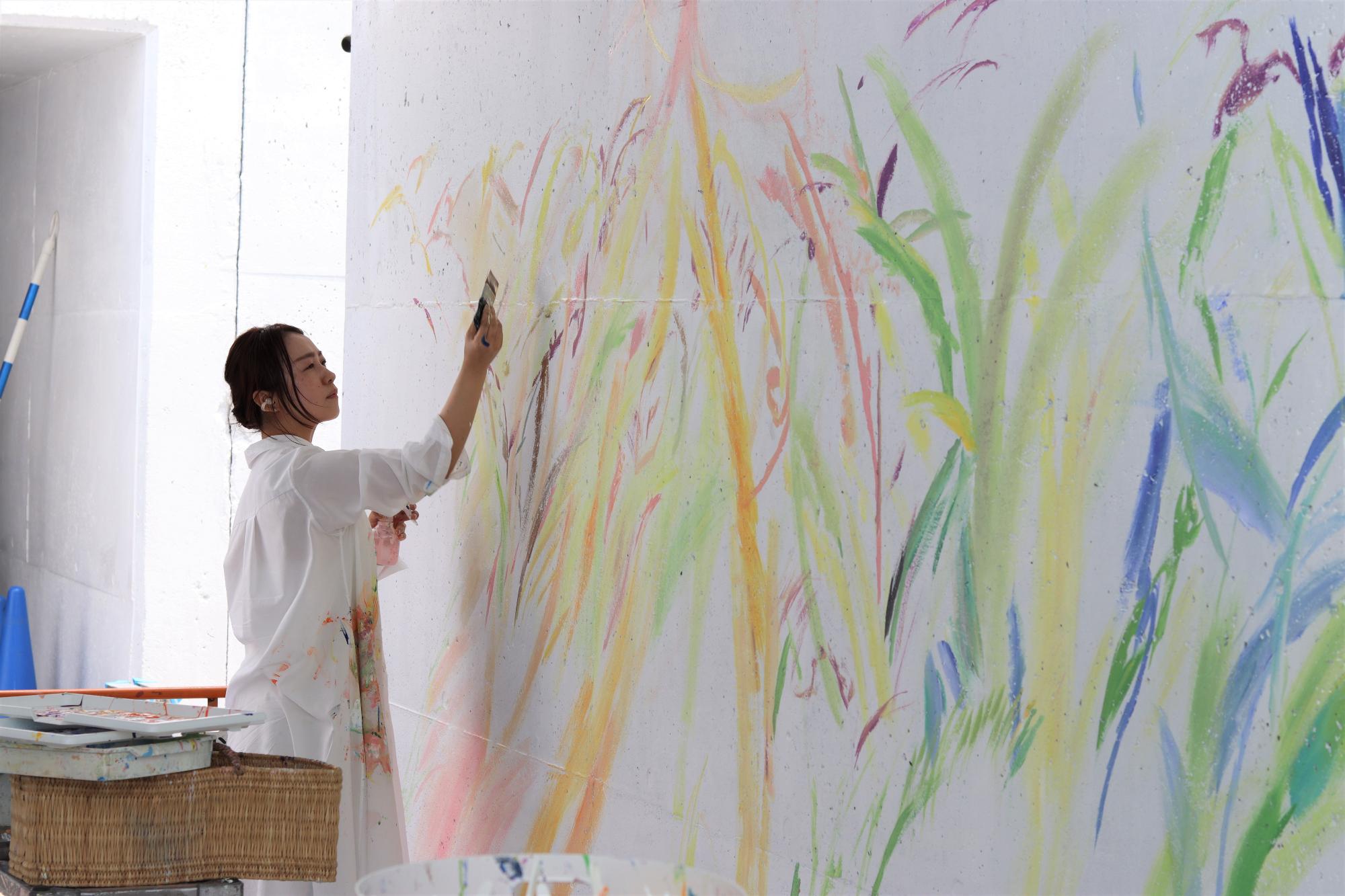 美術作家の植田志保さんが多彩な色づかいで壁画制作を進めている写真