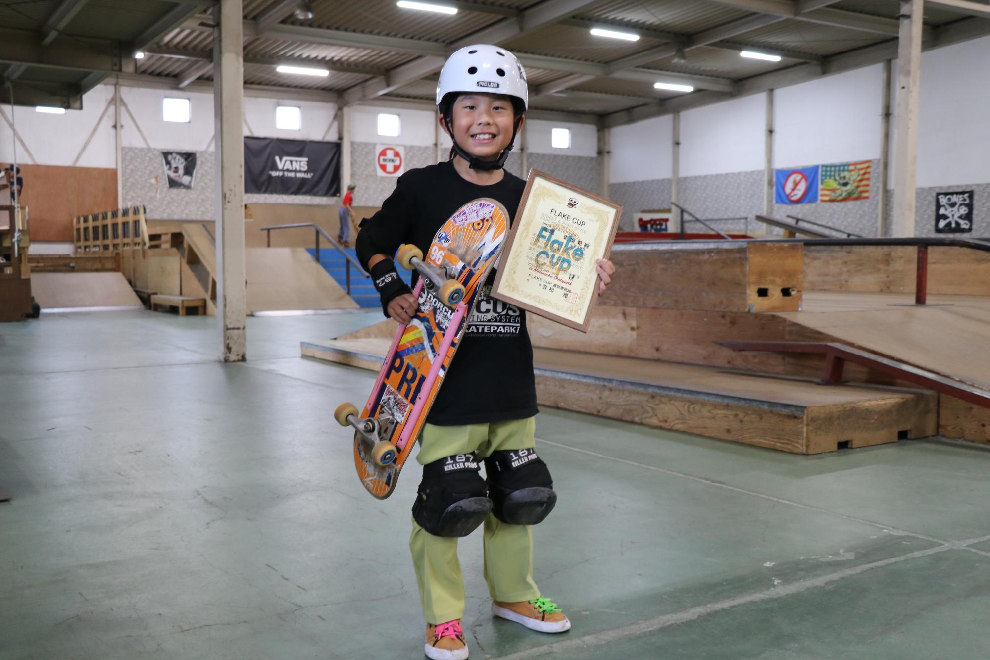 城下小学校3年の高尾吏優希さんが山崎町にあるヒナスケートパークの練習場内で賞状とスケートボードを手に笑顔を見せている写真