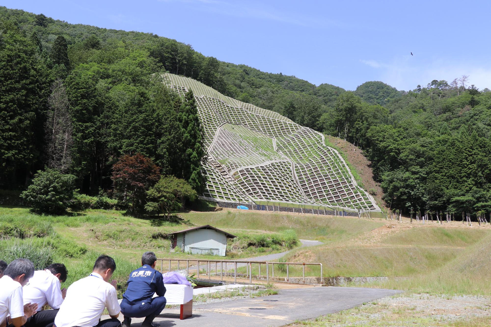 西日本豪雨による山崩れで一人が犠牲となった一宮町公文の現場で、福元市長が市幹部職員らとともに献花し、手を合わせている写真