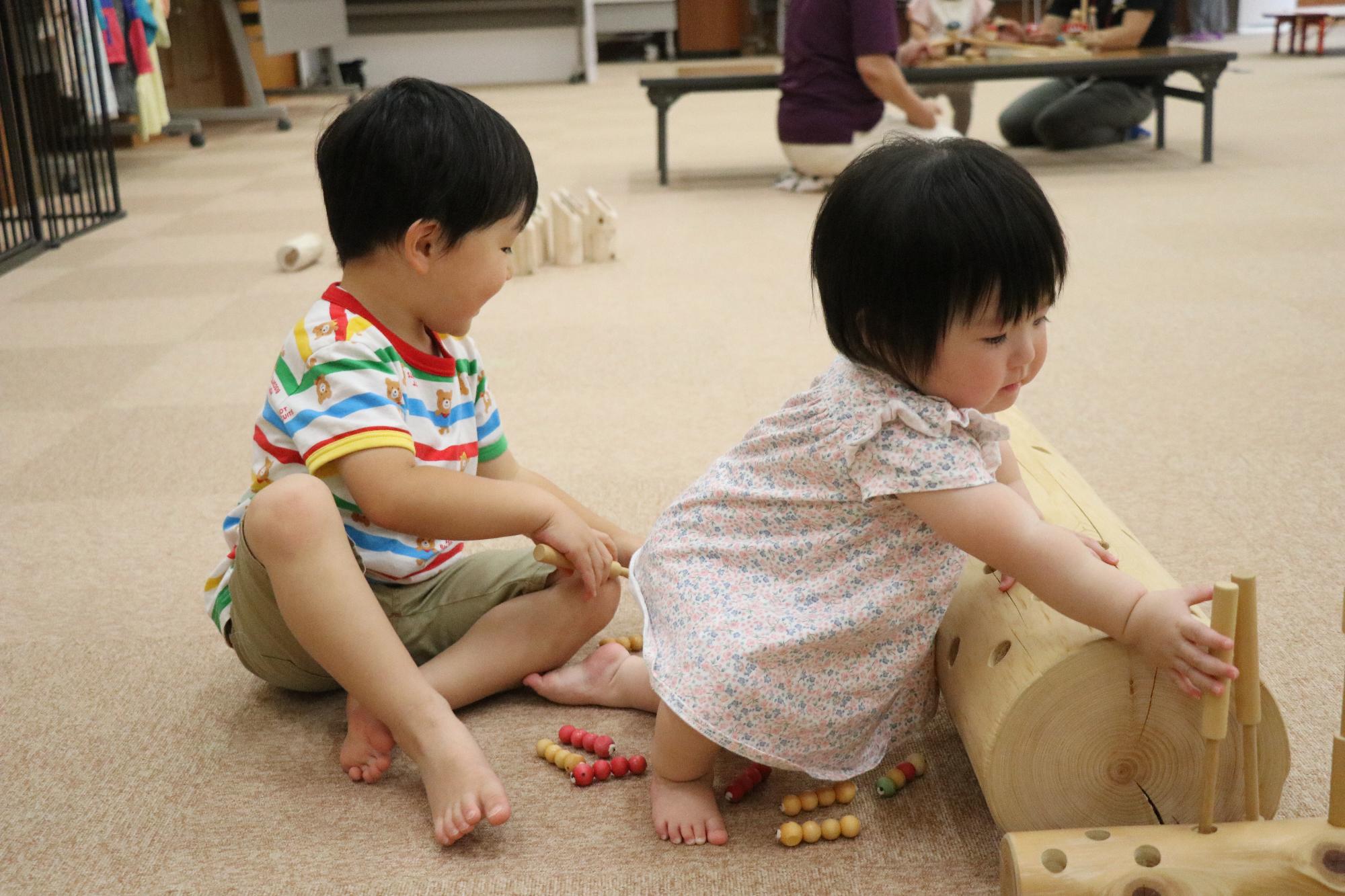 子ども二人が座って丸太型の木のおもちゃで遊んでいる写真