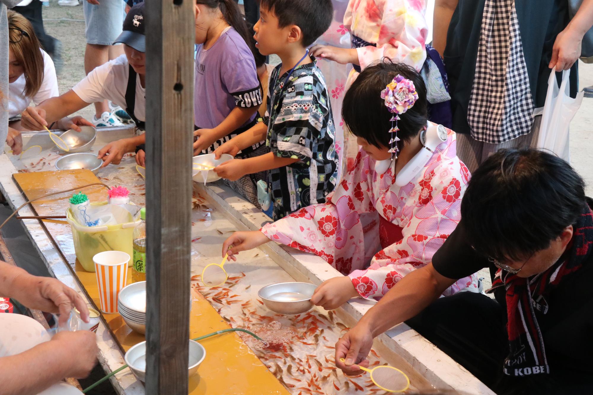 屋台で金魚すくいを楽しむ子どもたちの写真