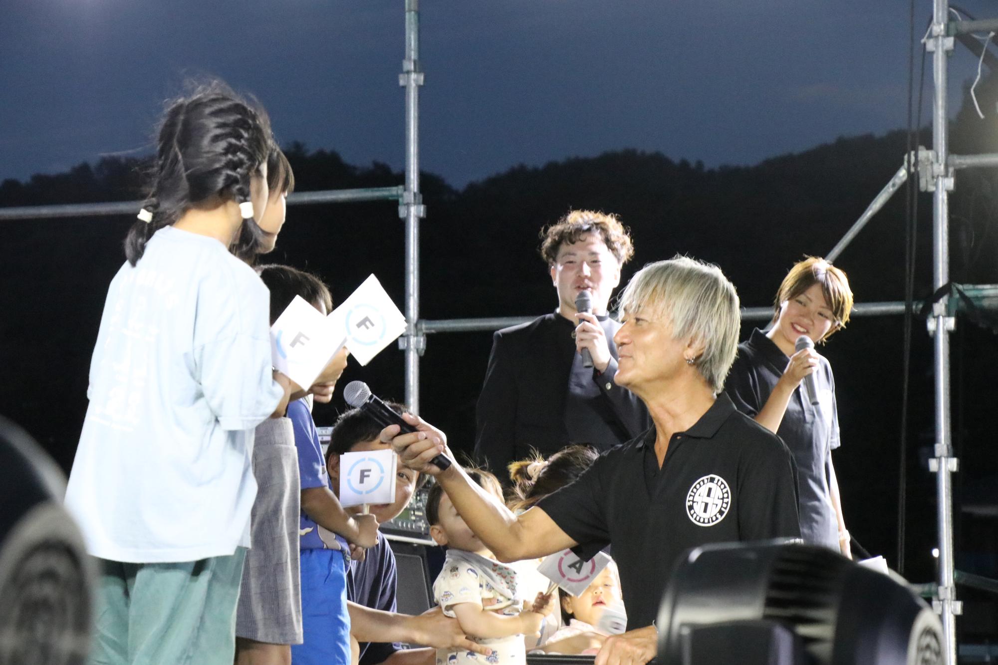 司会のターザン山下さんがステージで子どもにインタビューしている写真