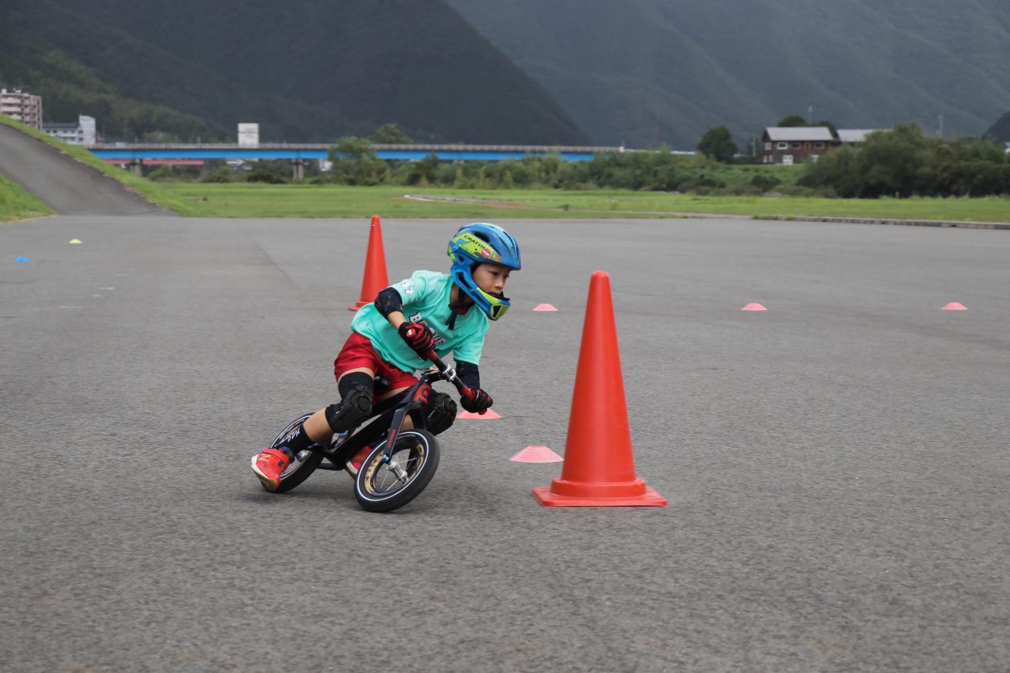 せせらぎ公園で植田さんがランバイクに乗ってカラーコーンの近くを曲がる練習をしている写真