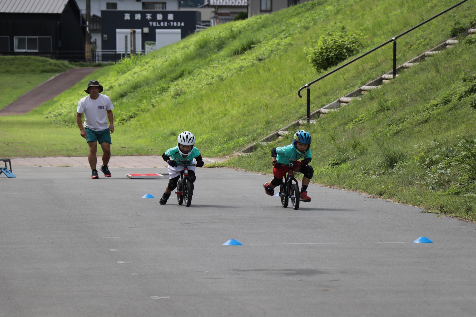 せせらぎ公園で植田さんと弟の瑛士さんがランバイクに乗り、直線のコースを走って競争している写真