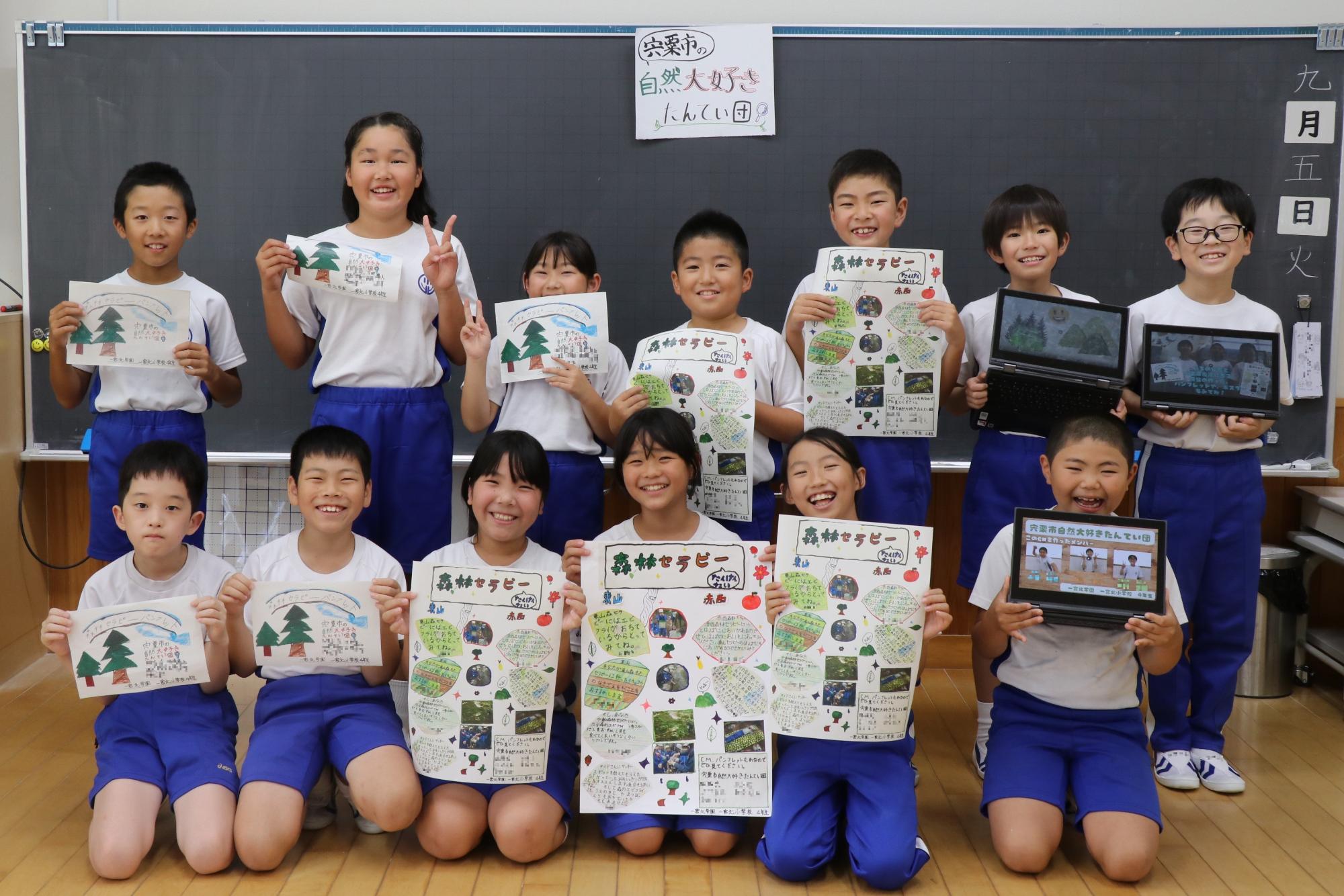 一宮北小学校4年生の13人が教室で、作成したパンフレットなどを手に持ち、2列に並んで笑顔を見せている写真