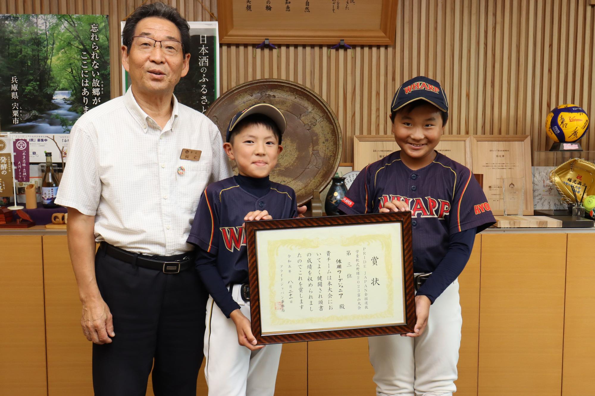 鎌田さんと寺田さんが全国3位の賞状を掲げ、福元市長と並んで正面を向いている写真