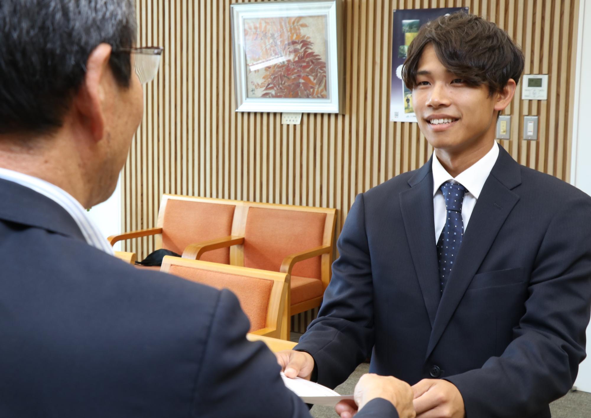 市長室で市長と田中さんが向き合い、田中さんが市長から委嘱状を受け取っている写真
