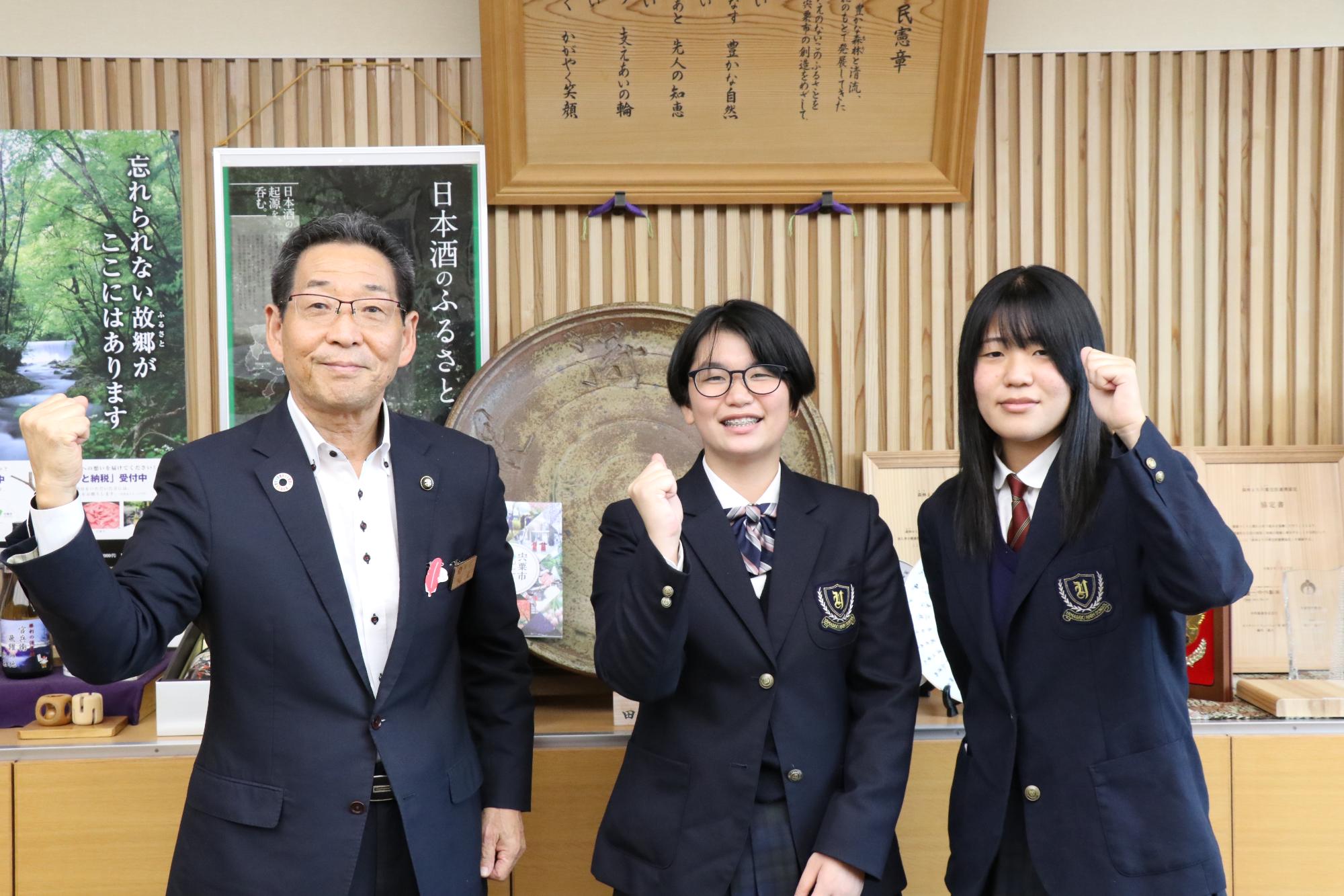 左から順に福元市長、金持さん、秦さんが市長室でガッツポーズをして並んで立っている写真