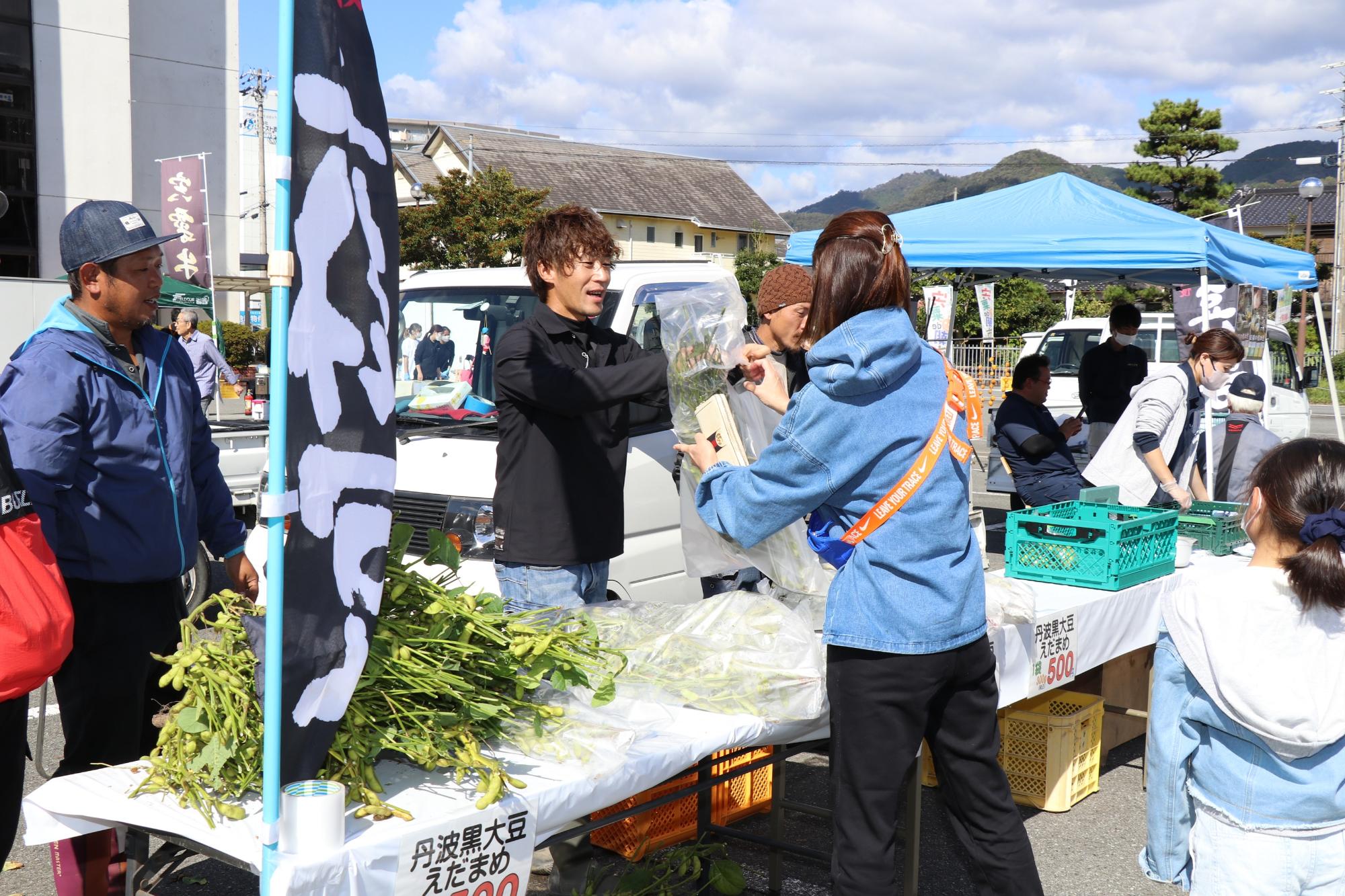 ブースに農家が生産した丹波黒大豆の枝豆が並び、それを客が買い求めている写真