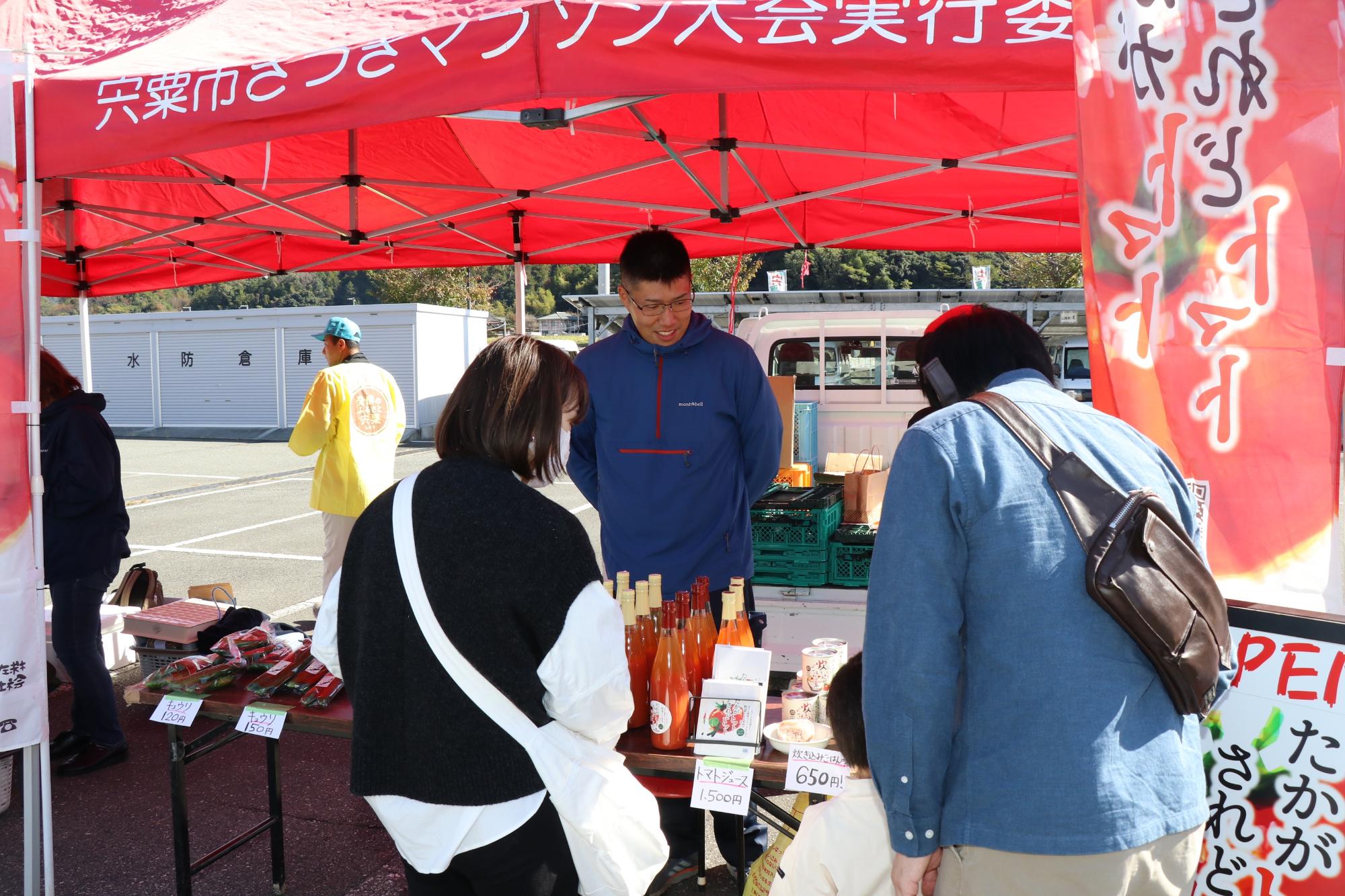 トマトやキュウリなどを買い求める客と応対する生産者の写真