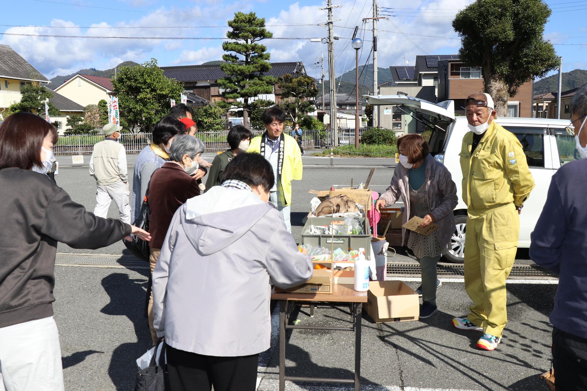 野菜などを買い求める複数人の客と応対する生産者の写真