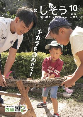 県立国見の森公園であった「くにみまつり」の丸太切り体験で、丸太を横から支える人と鋸を前後に動かして木を切っている子どもの写真