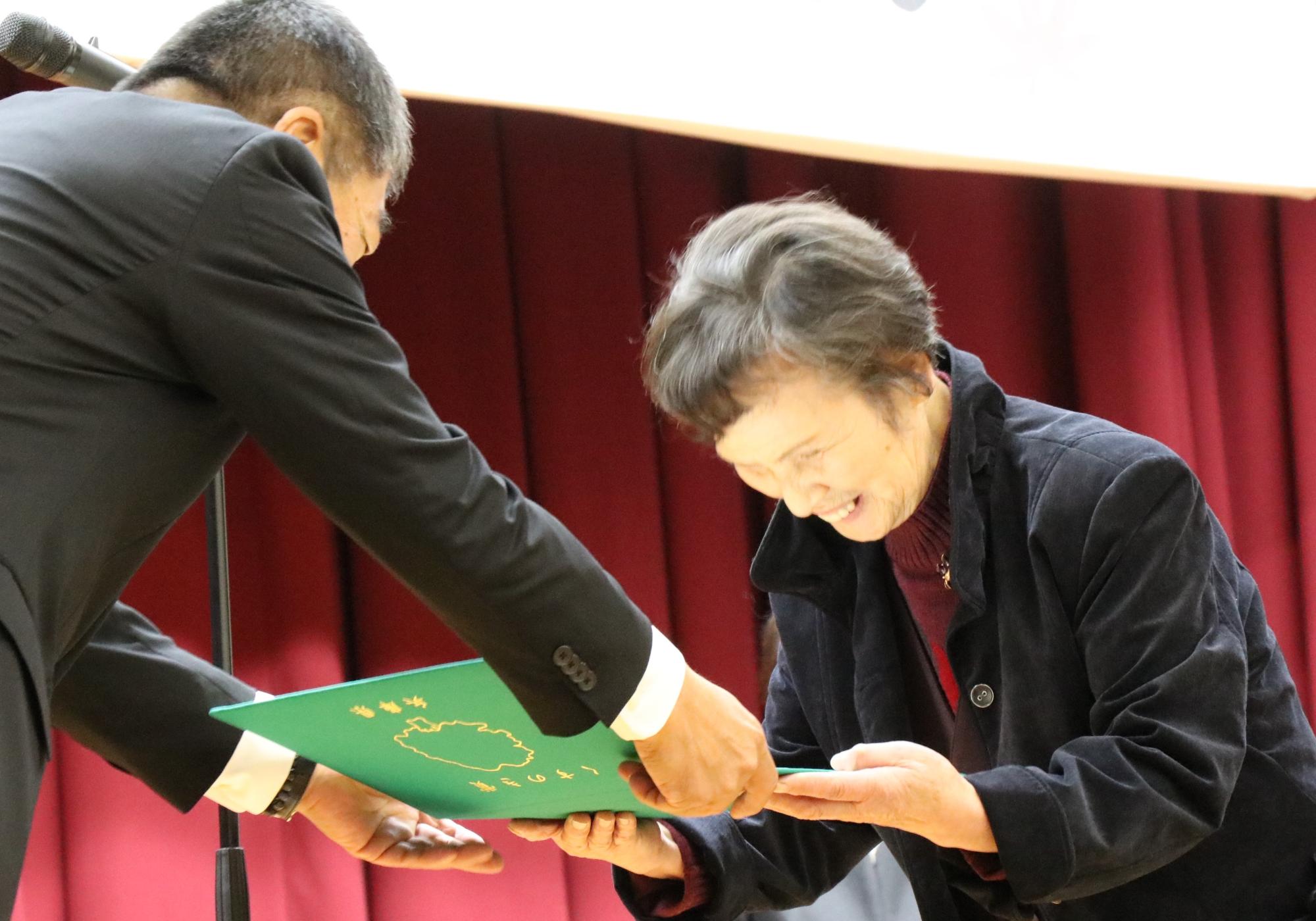 朗読ボランティアふきのとう山崎代表の古河道子さんが西播磨県民局長からくすのき賞の賞状を受け取っている画像