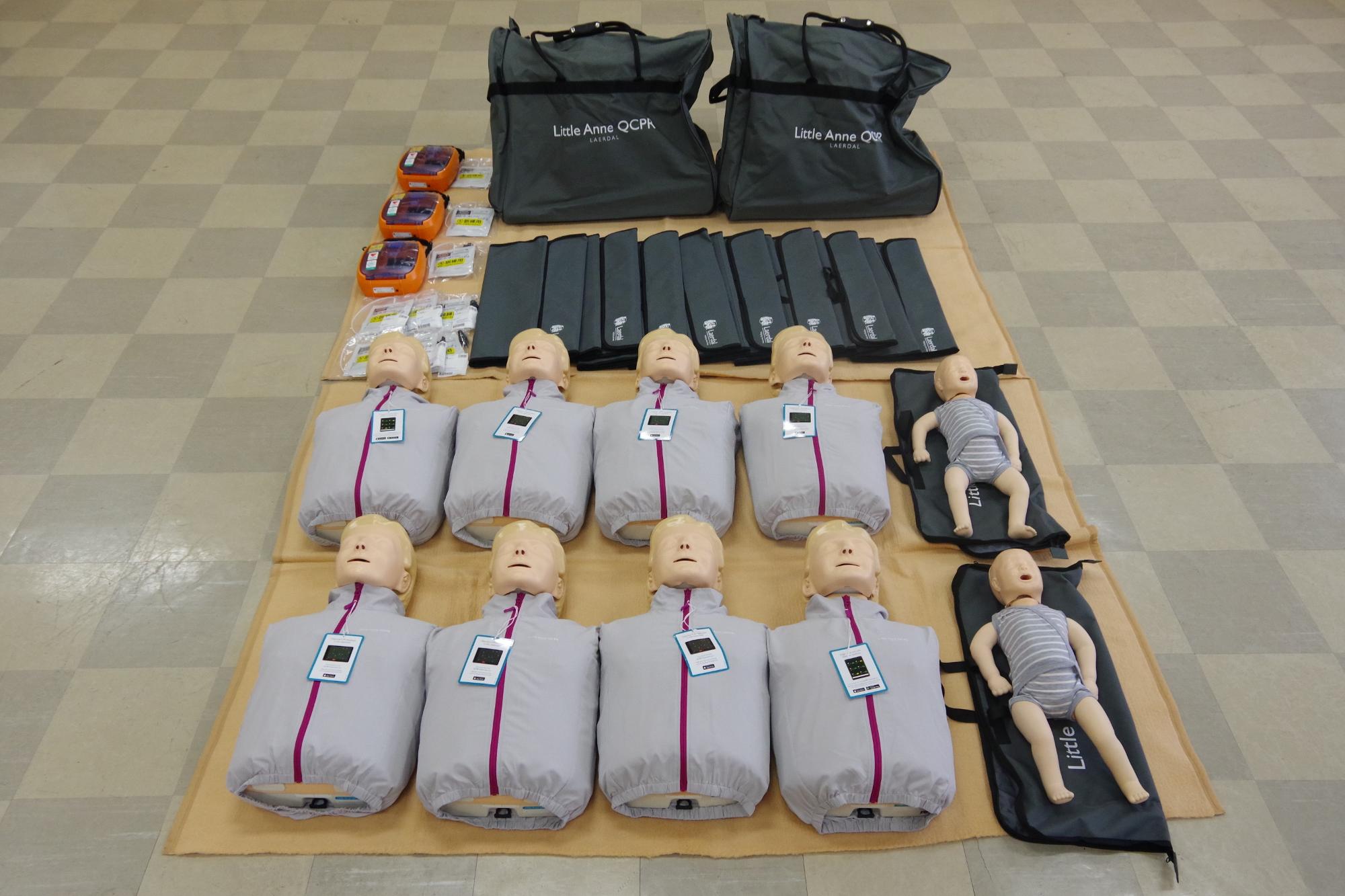 寄贈のあった訓練用の人形とAEDトレーナーが床に並べられている写真