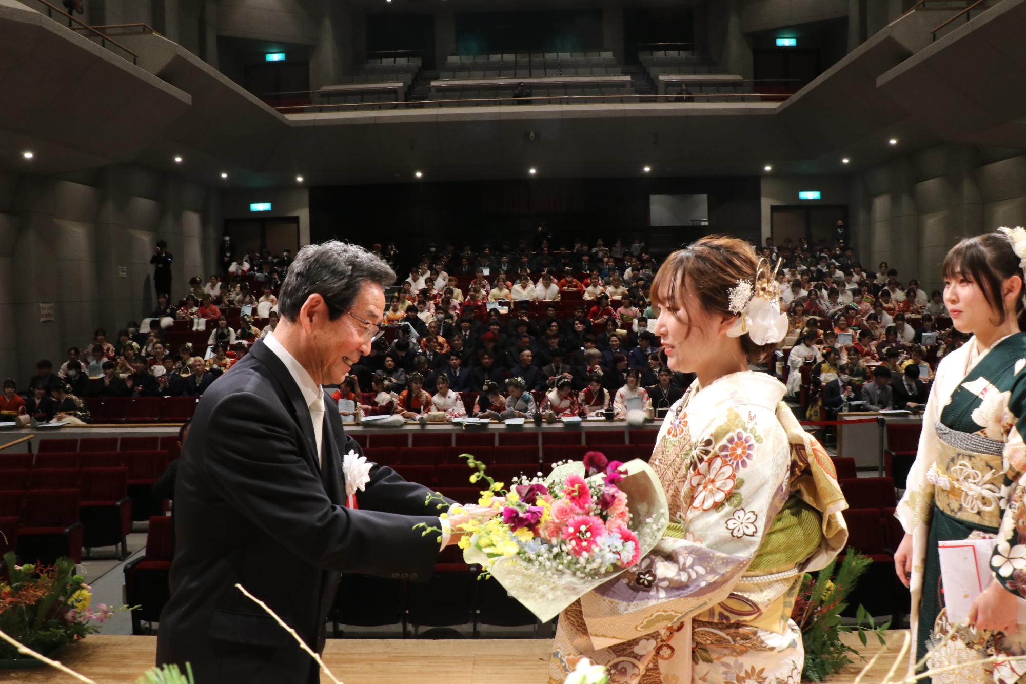 山崎文化会館のステージ上で新成人を代表して、市長からお祝いの花束を受け取る鳥居優里さん