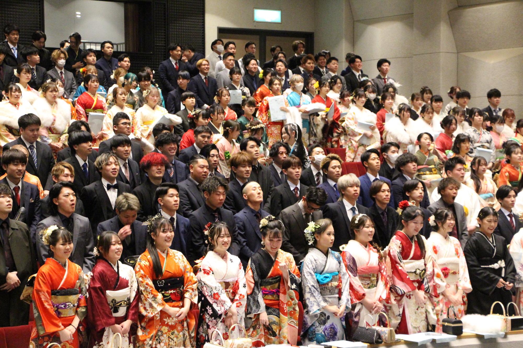 山崎文化会館ホールで式典に臨む20歳の新成人らが並んで立っている写真