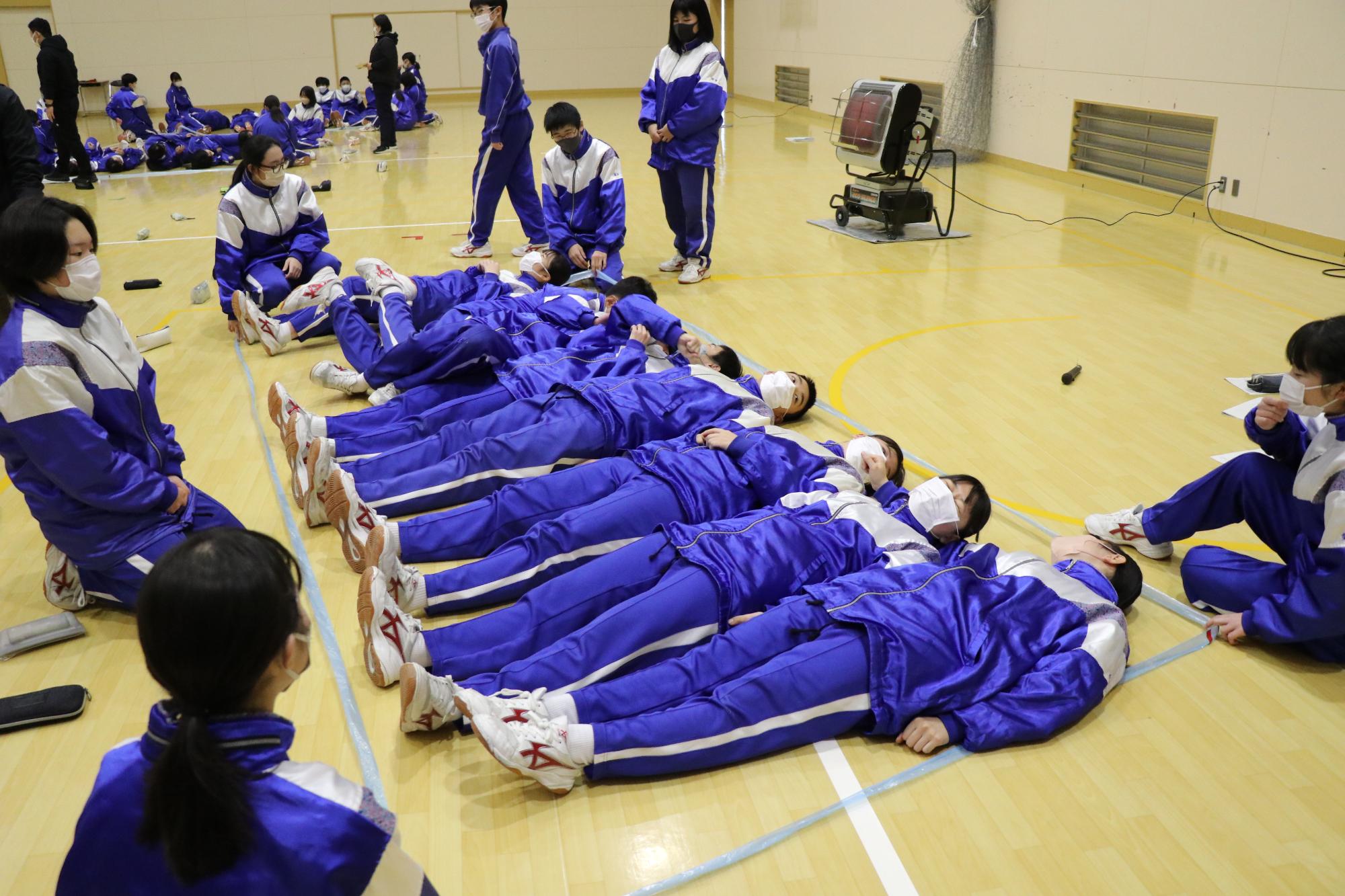 山崎南中学校の生徒8人が体育館で8平方メートルに区切られたスペースに寝ころんでいる写真