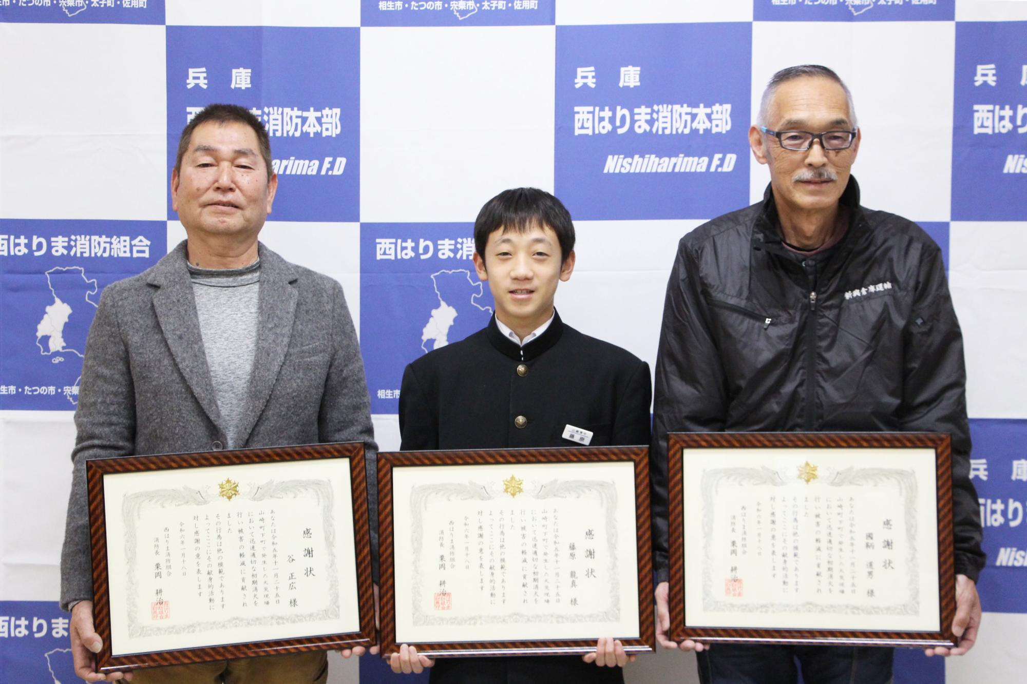 宍粟消防署で谷さん、藤原さん、国鞆さんが感謝状をかかげ横一列に並び、笑顔を見せている写真